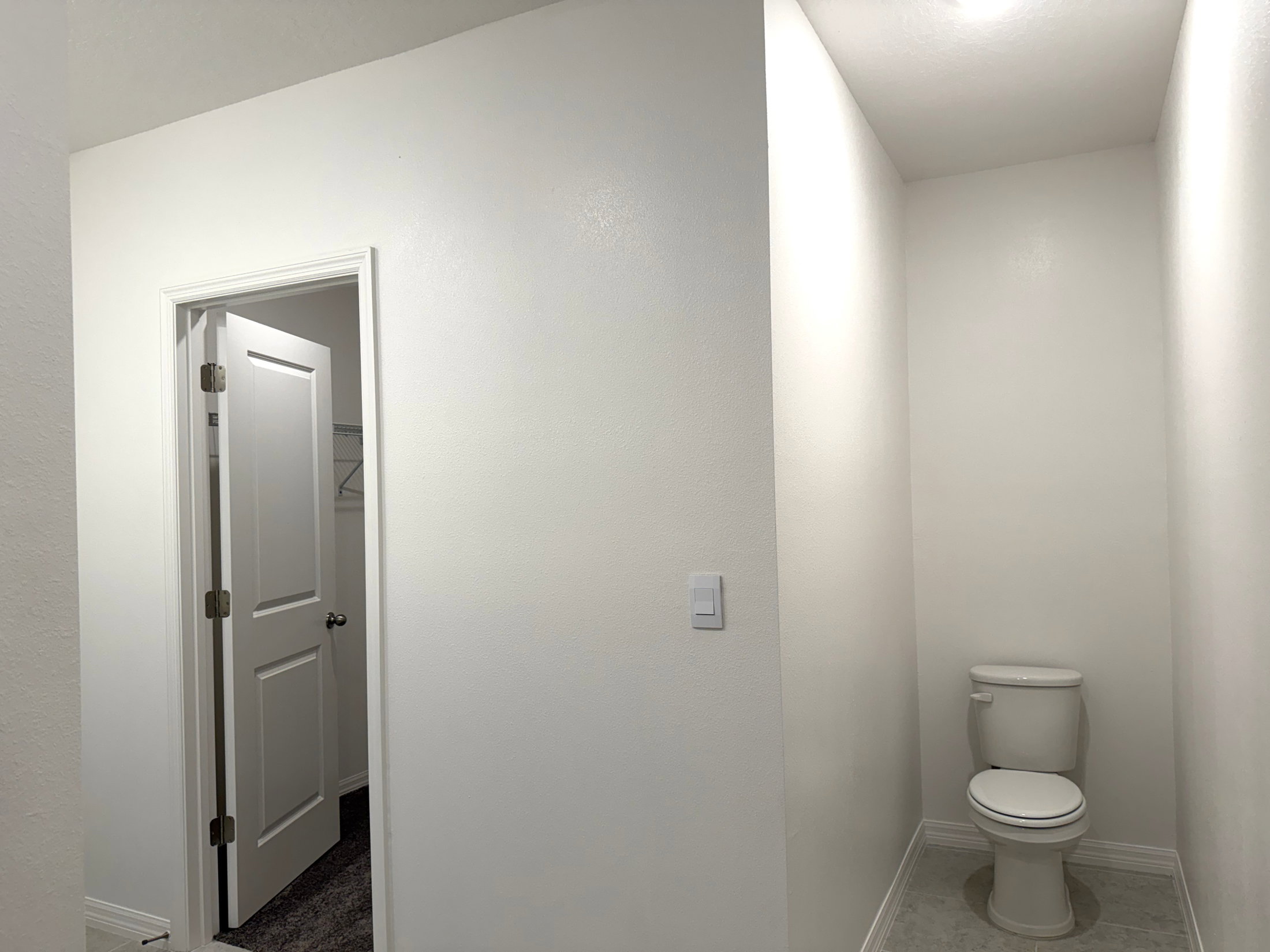A small, clean bathroom with a white toilet and a door leading to another room.