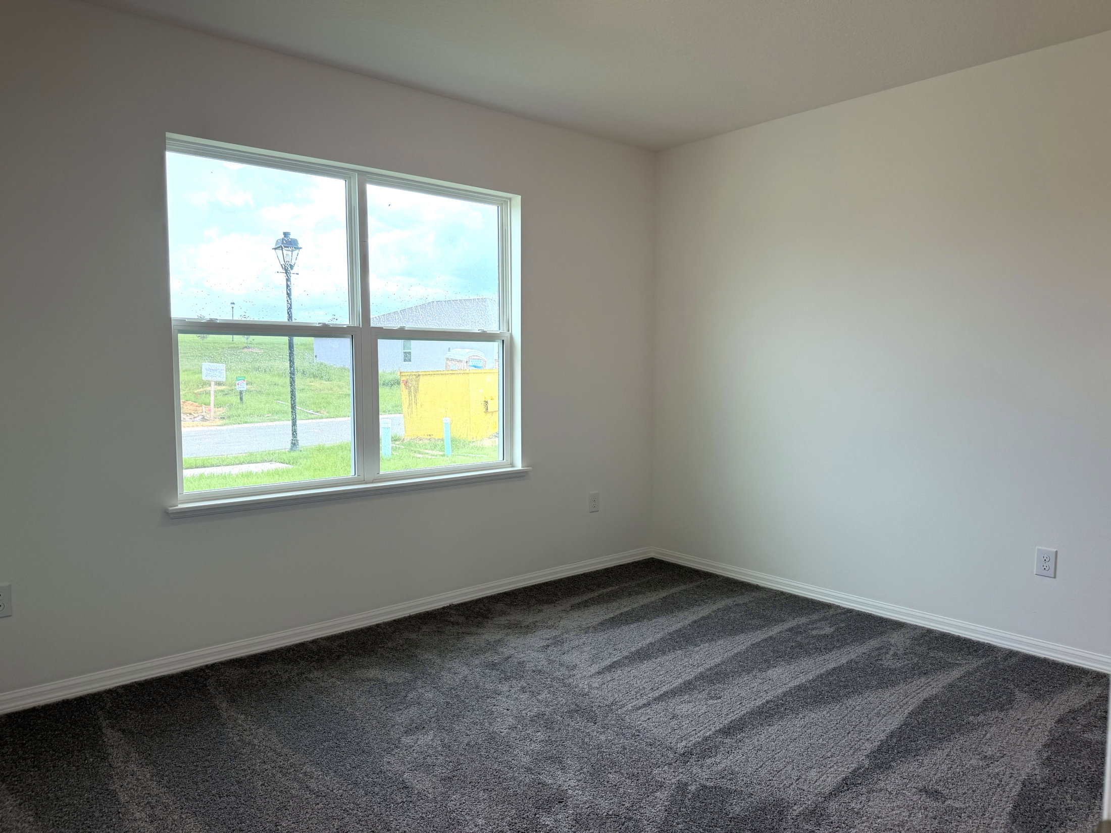 A empty room with gray carpet and a large window letting in natural light.