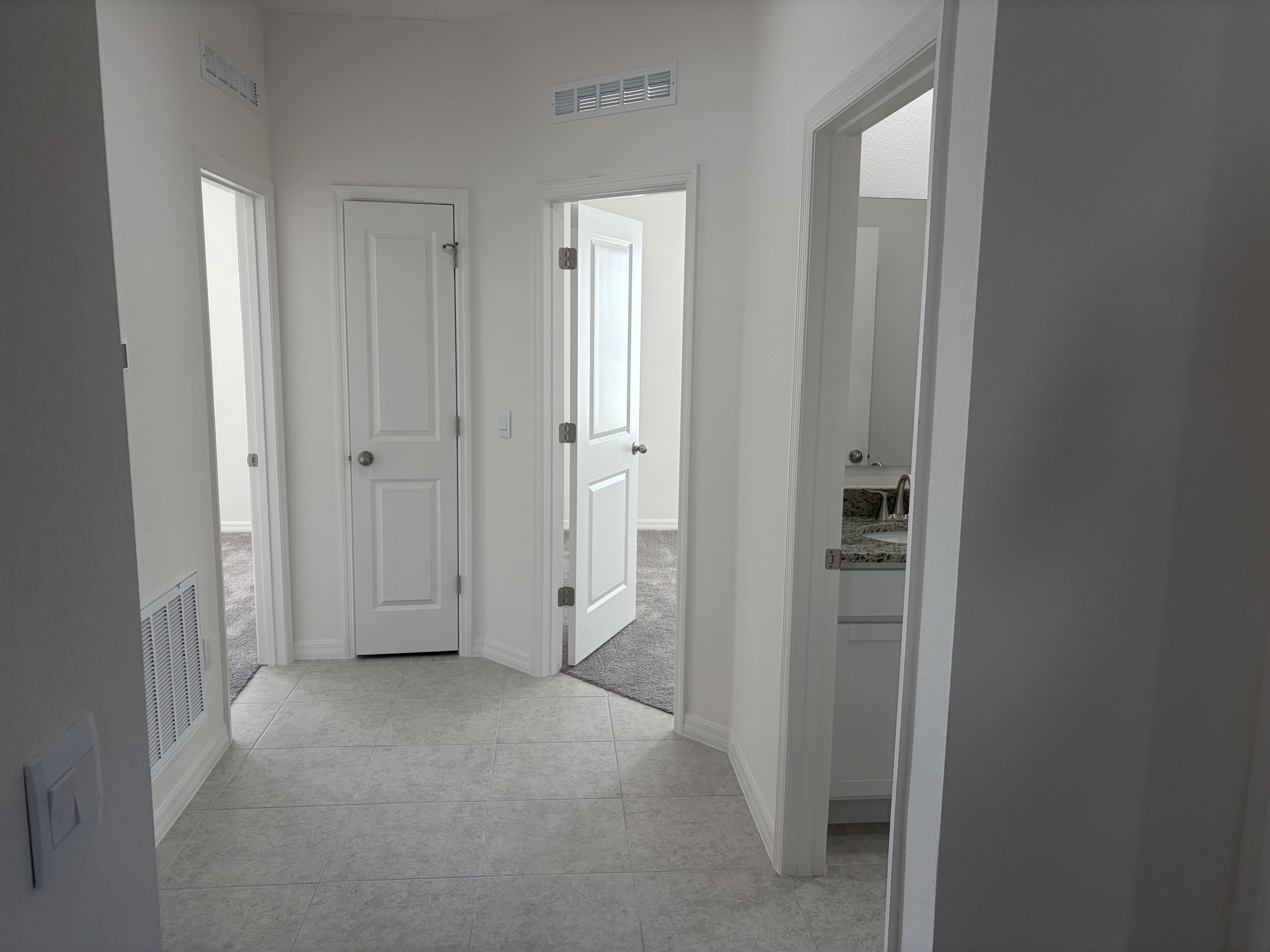 A bright, open hallway featuring multiple white doors leading to rooms in a modern home with tile flooring and neutral-colored walls.