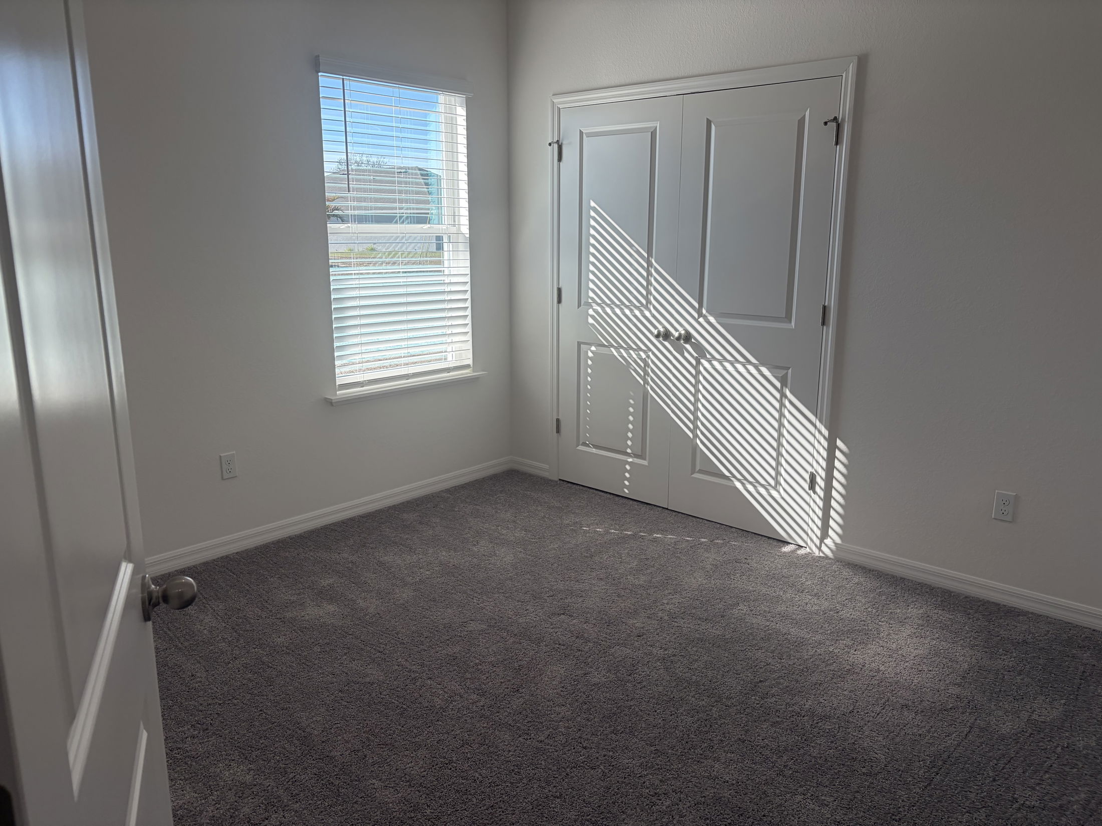 Bright, spacious bedroom featuring carpet flooring, a closet with double doors, and natural light streaming through window blinds.