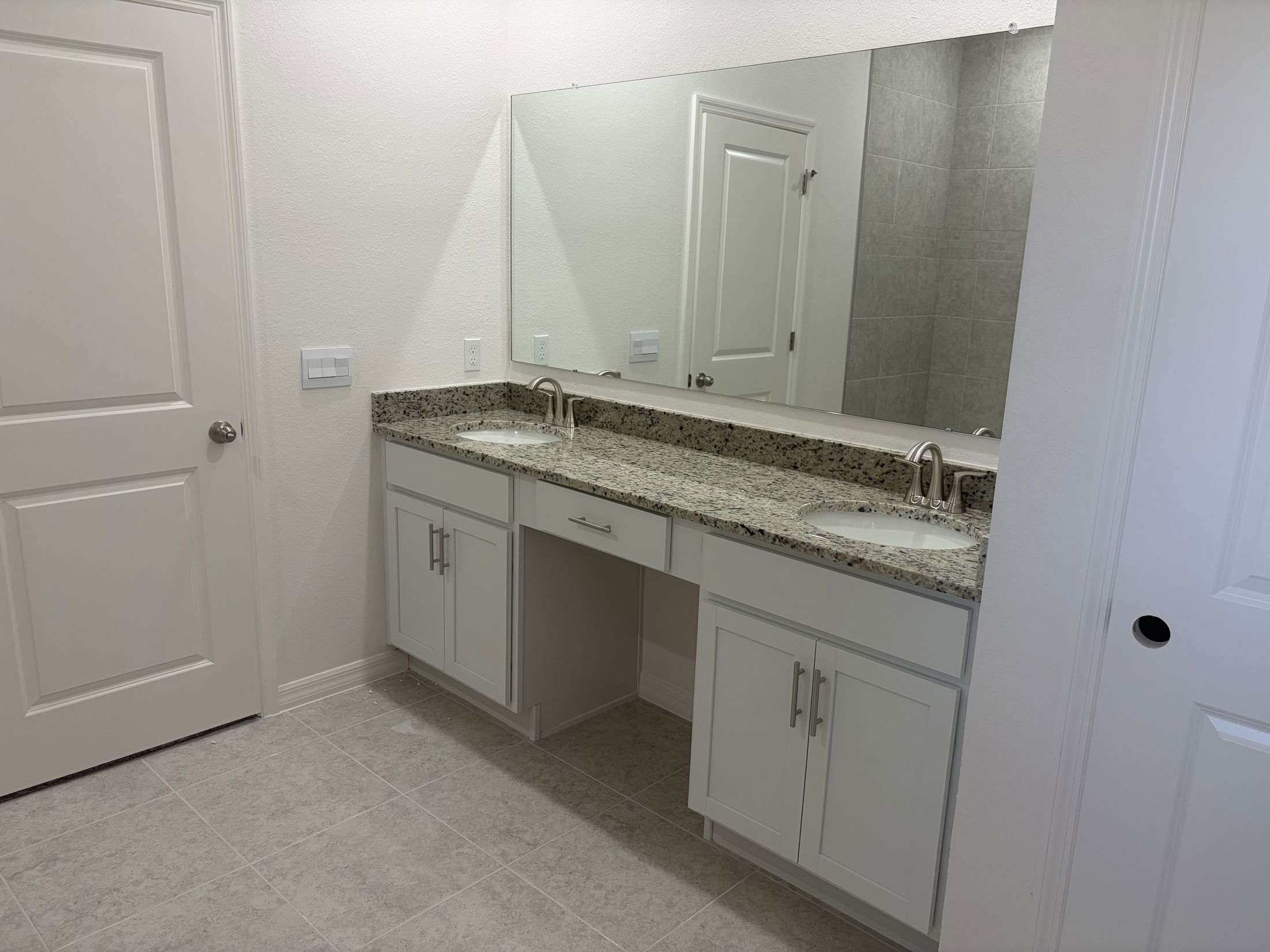 Modern bathroom interior featuring a dual sink vanity with granite countertop and a large mirror in a bright, neutral color scheme.