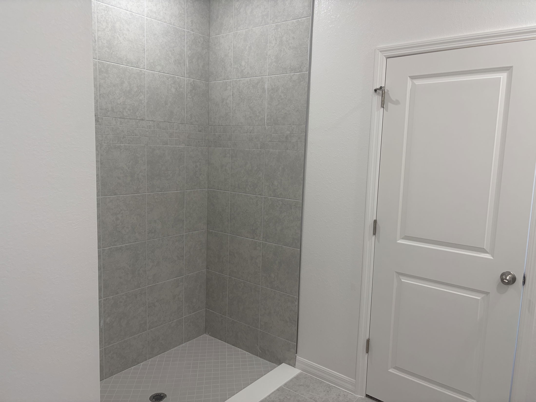 Modern bathroom featuring a gray tiled shower area and a white door.