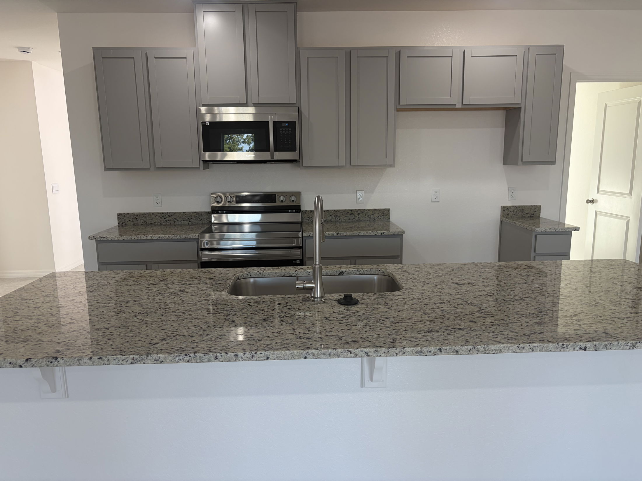 Modern kitchen design featuring gray cabinetry, stainless steel appliances, and granite countertops.