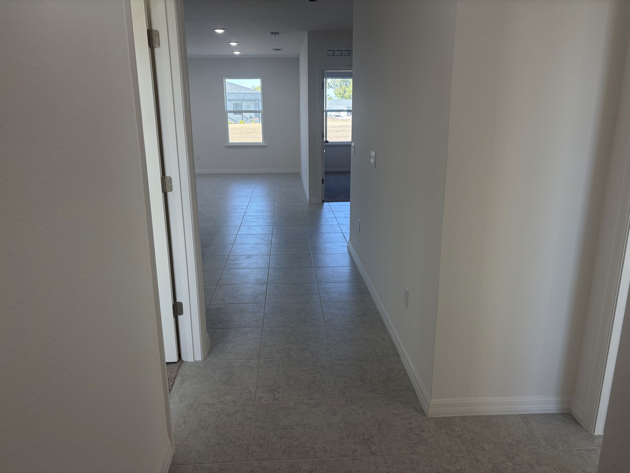 A bright and spacious hallway leading to a sunlit room in a modern home interior with tiled floors.