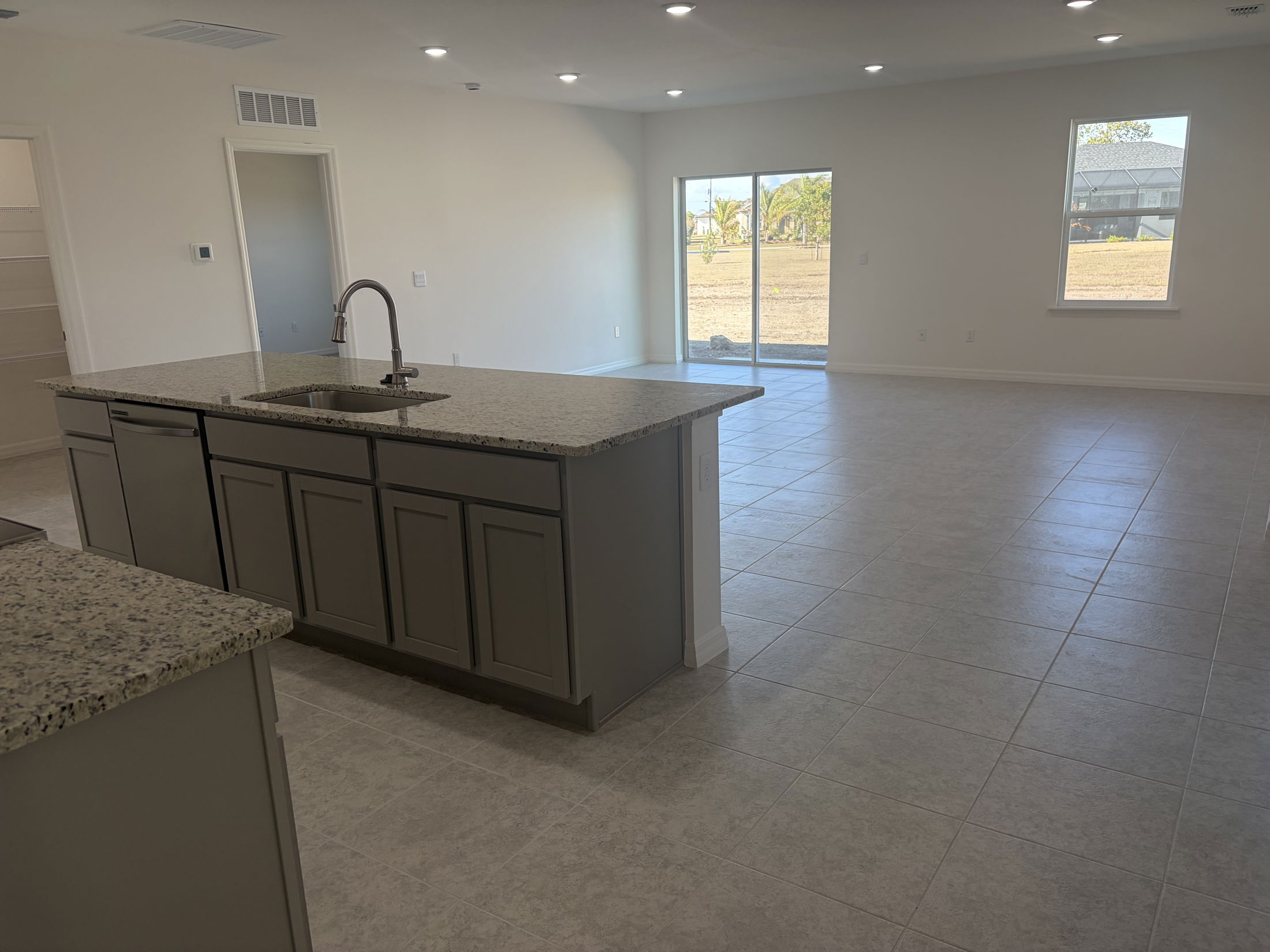 Modern open-concept kitchen with granite countertops and tile flooring leading to a bright living area with large windows.