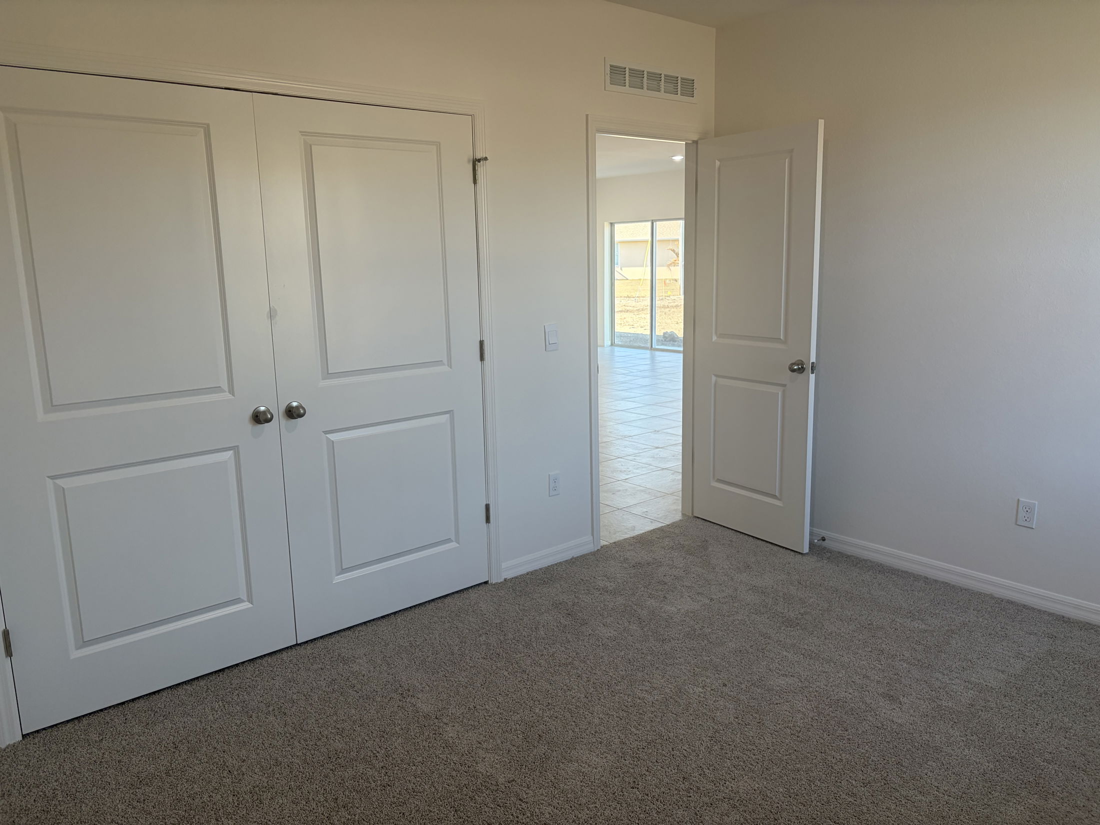 Bright and spacious empty bedroom featuring double white closet doors and a doorway leading to a sunlit room.
