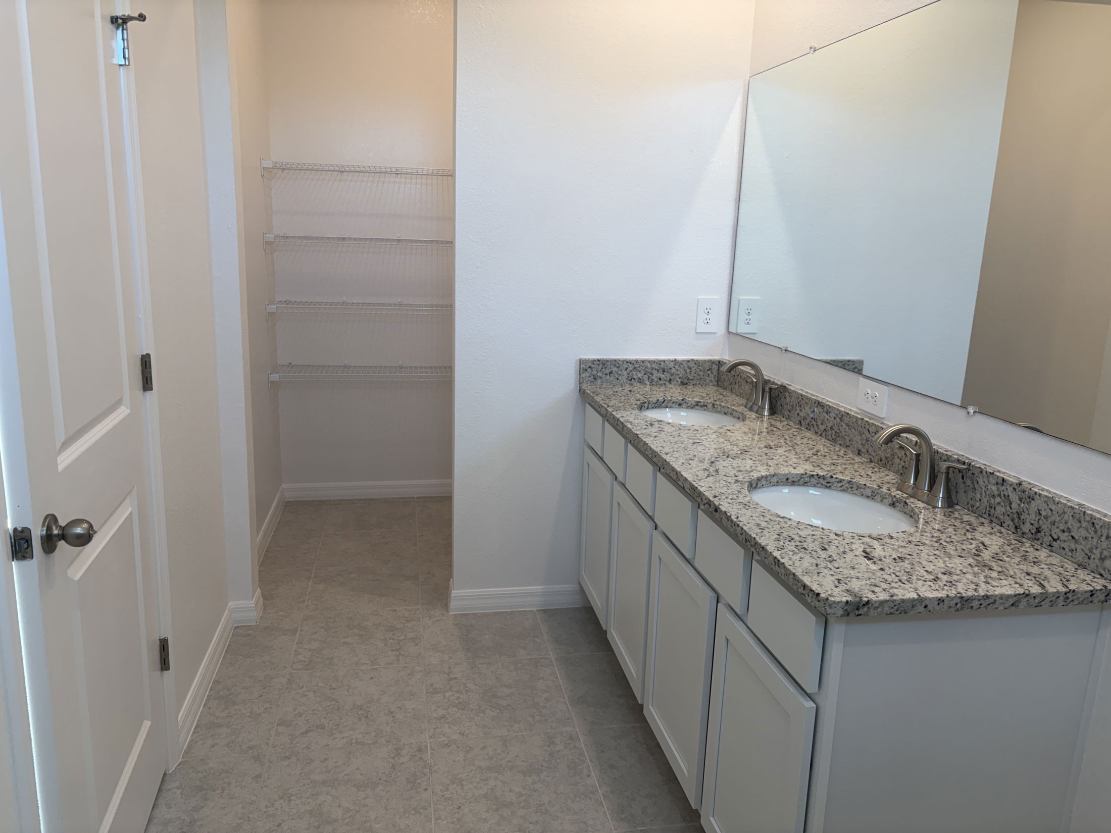 Modern bathroom featuring a double sink vanity with granite countertop and a spacious closet with wire shelving.