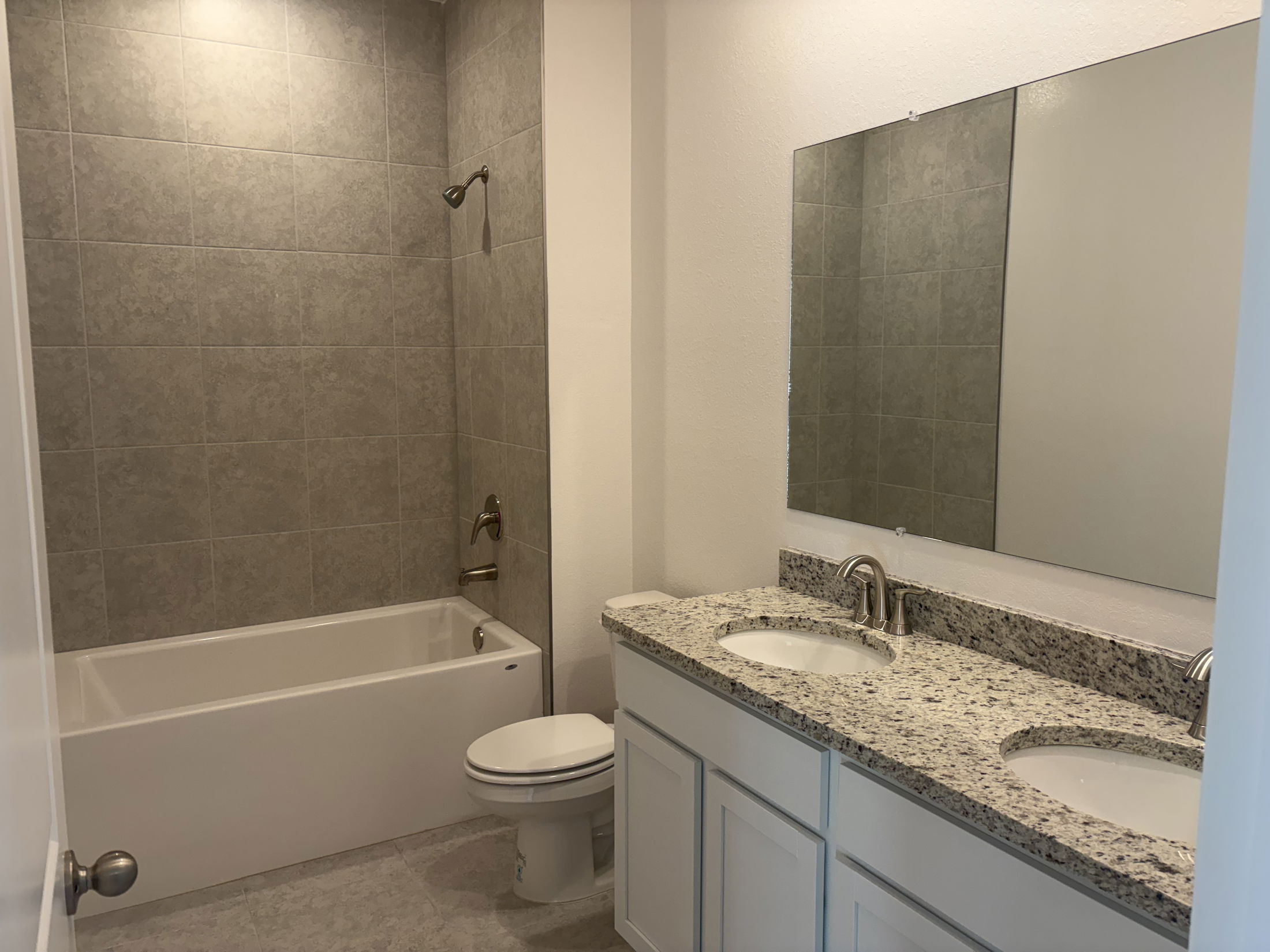 Modern bathroom featuring a spacious double sink vanity, grey tile walls, a shower and bathtub combination, and ambient overhead lighting.