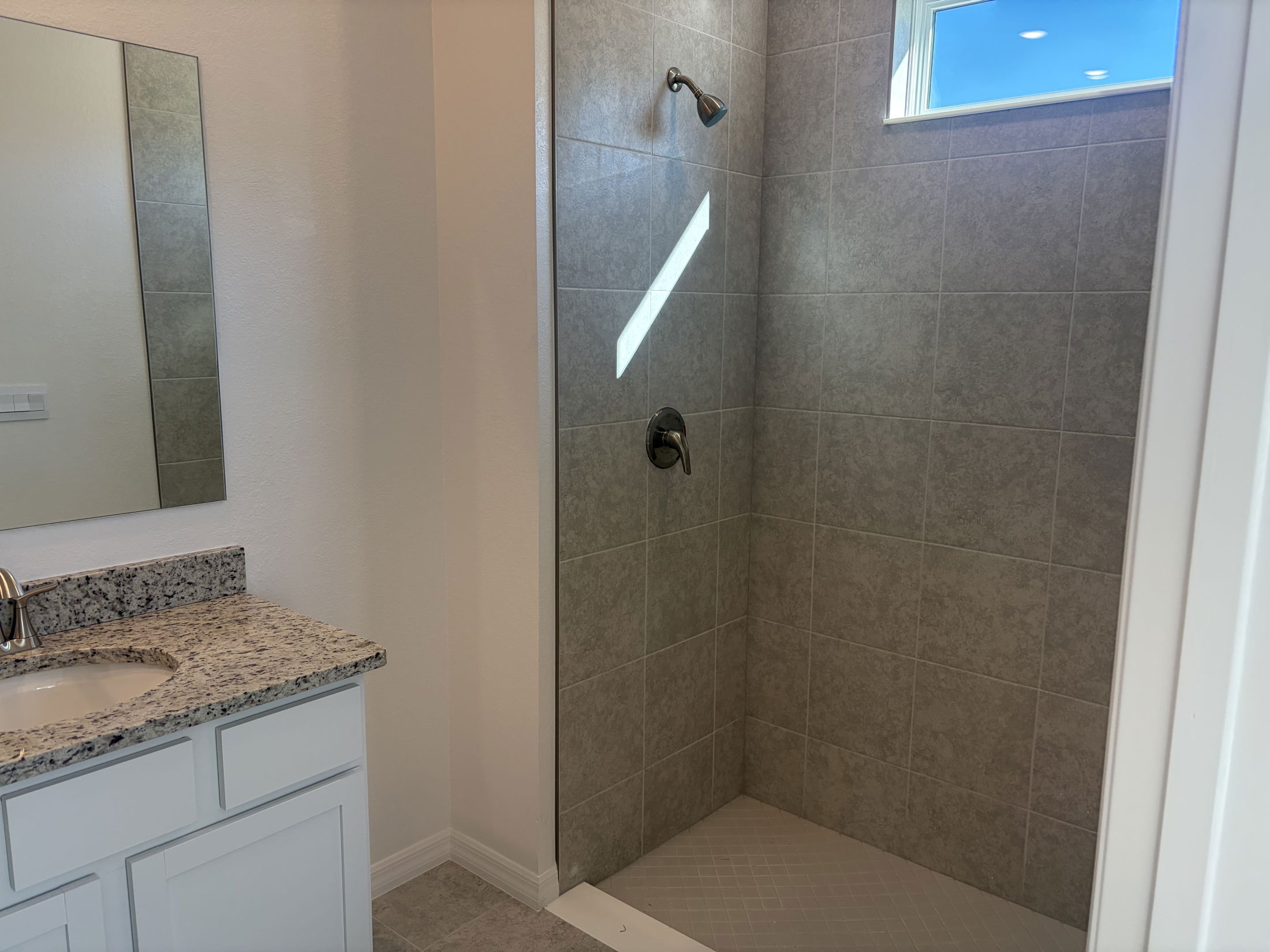 Modern bathroom featuring a spacious shower with gray tile, a stone countertop, and a large mirror.
