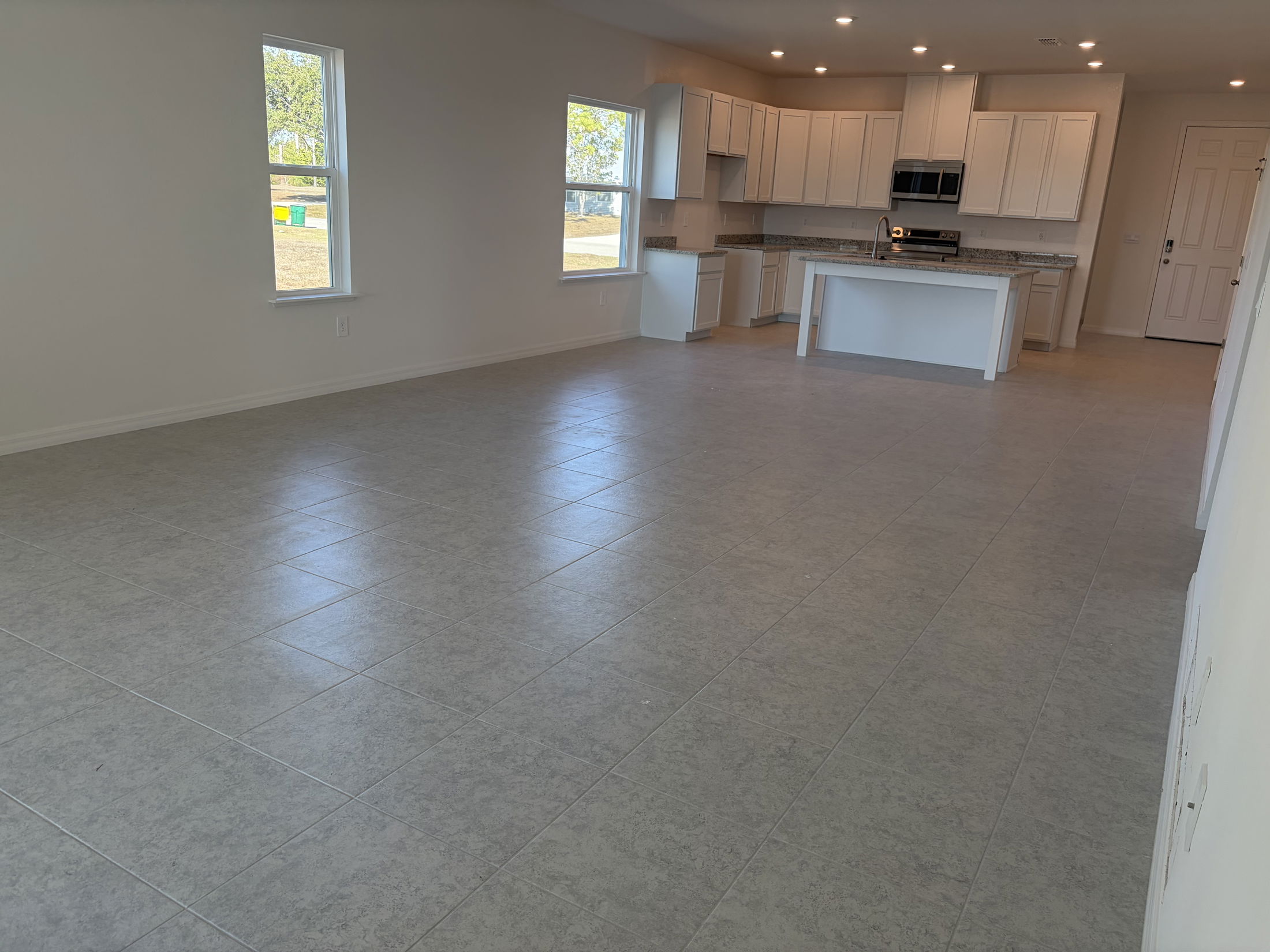 Spacious modern living room with tiled floor and large windows in a newly constructed home.