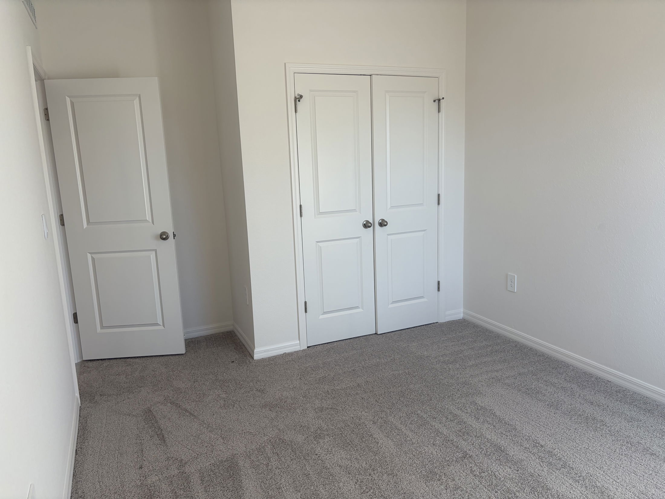 Bright and spacious room with light gray carpet and white double closet doors.