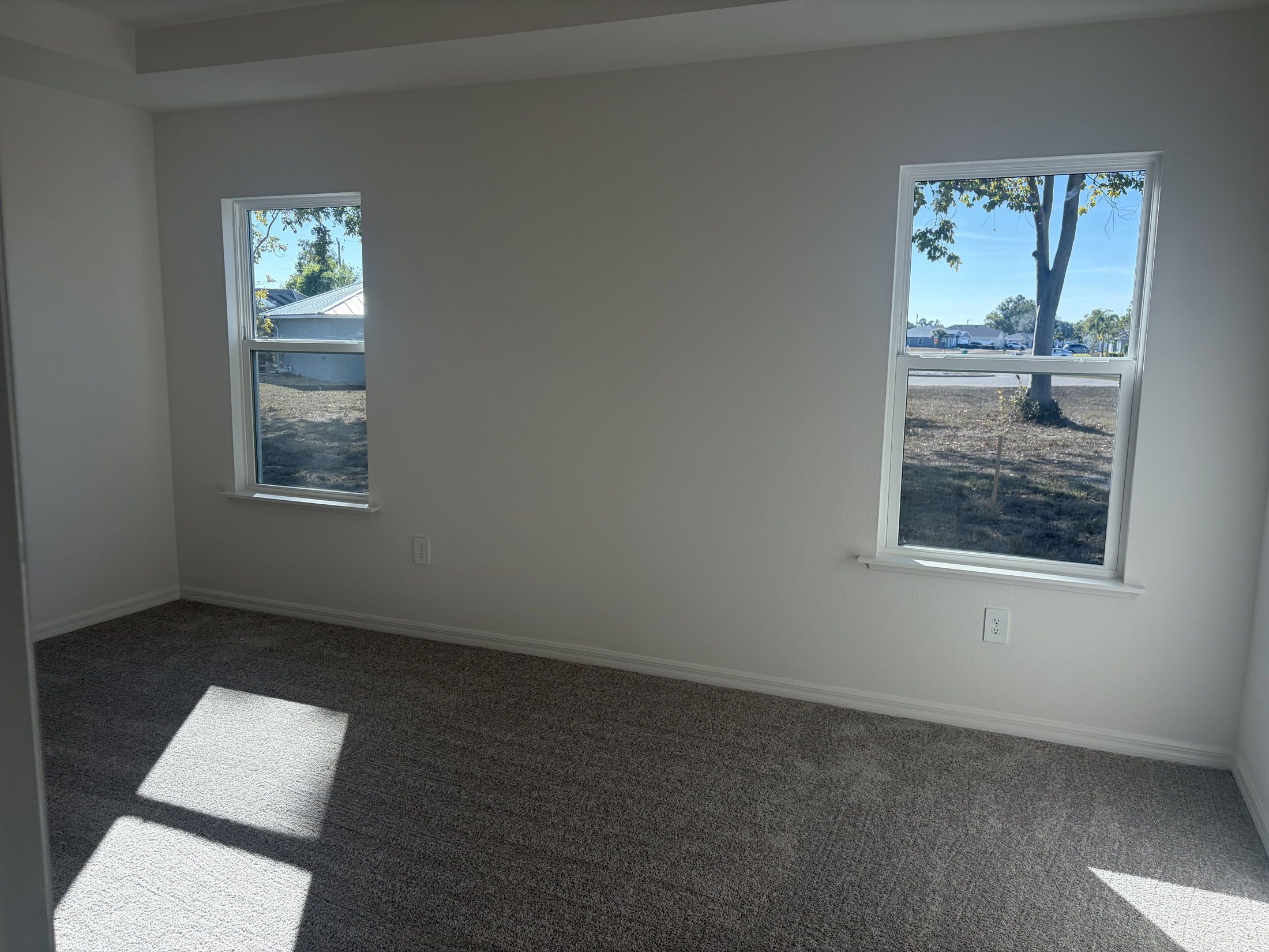 Bright and spacious empty room with two windows allowing natural light and a view of the outdoors.
