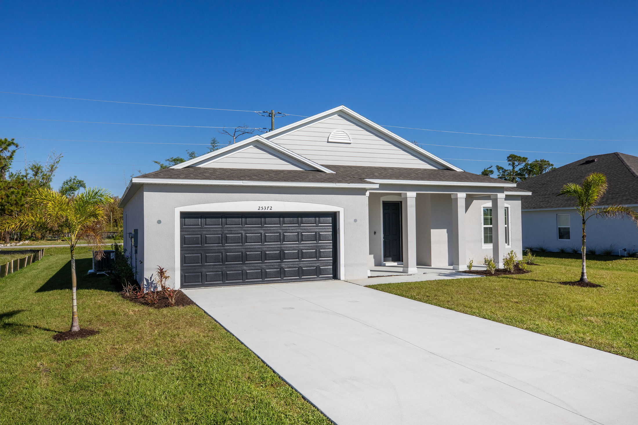 Modern single-story white house with a two-car garage and a manicured lawn under a clear blue sky.