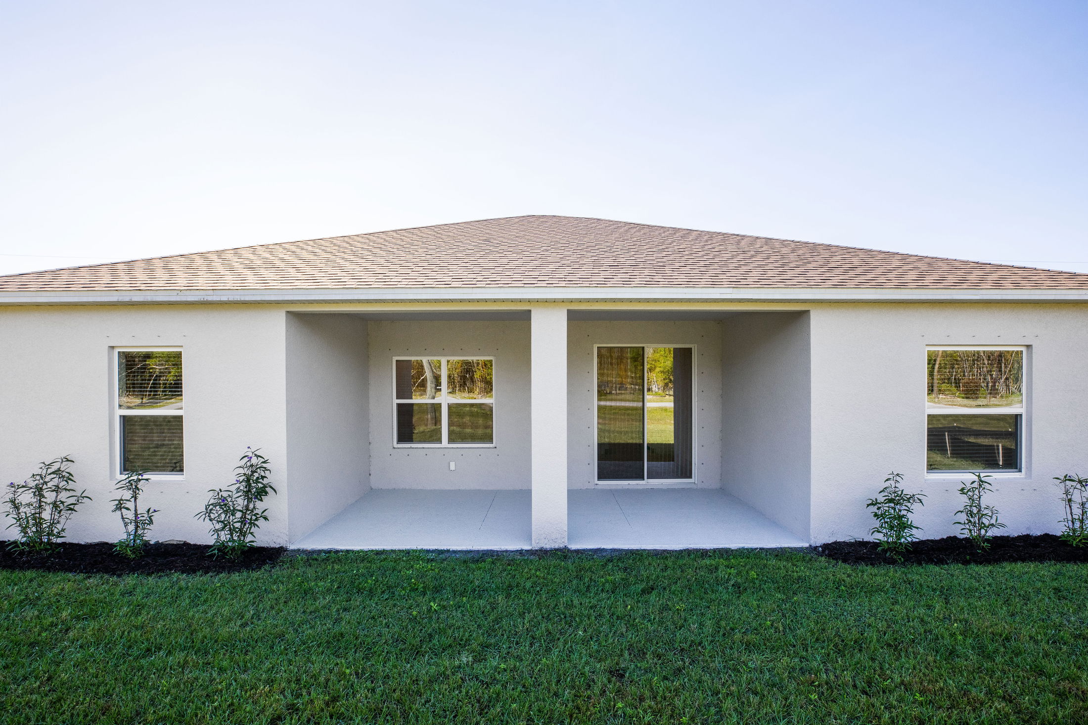Modern single-story house exterior with a covered patio, large windows, and a well-maintained lawn.