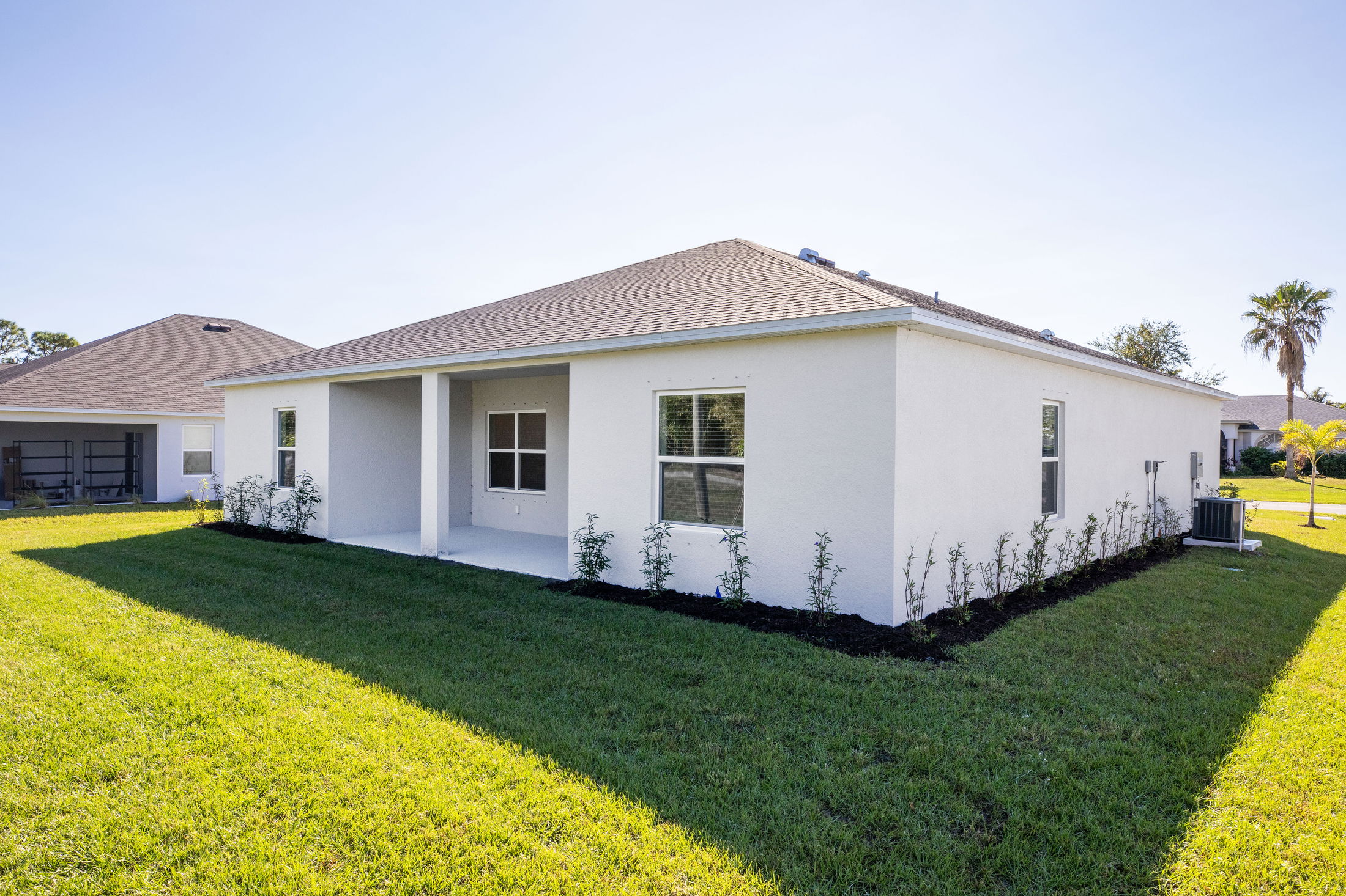 Modern single-story white house with manicured lawn and covered porch in a suburban neighborhood.