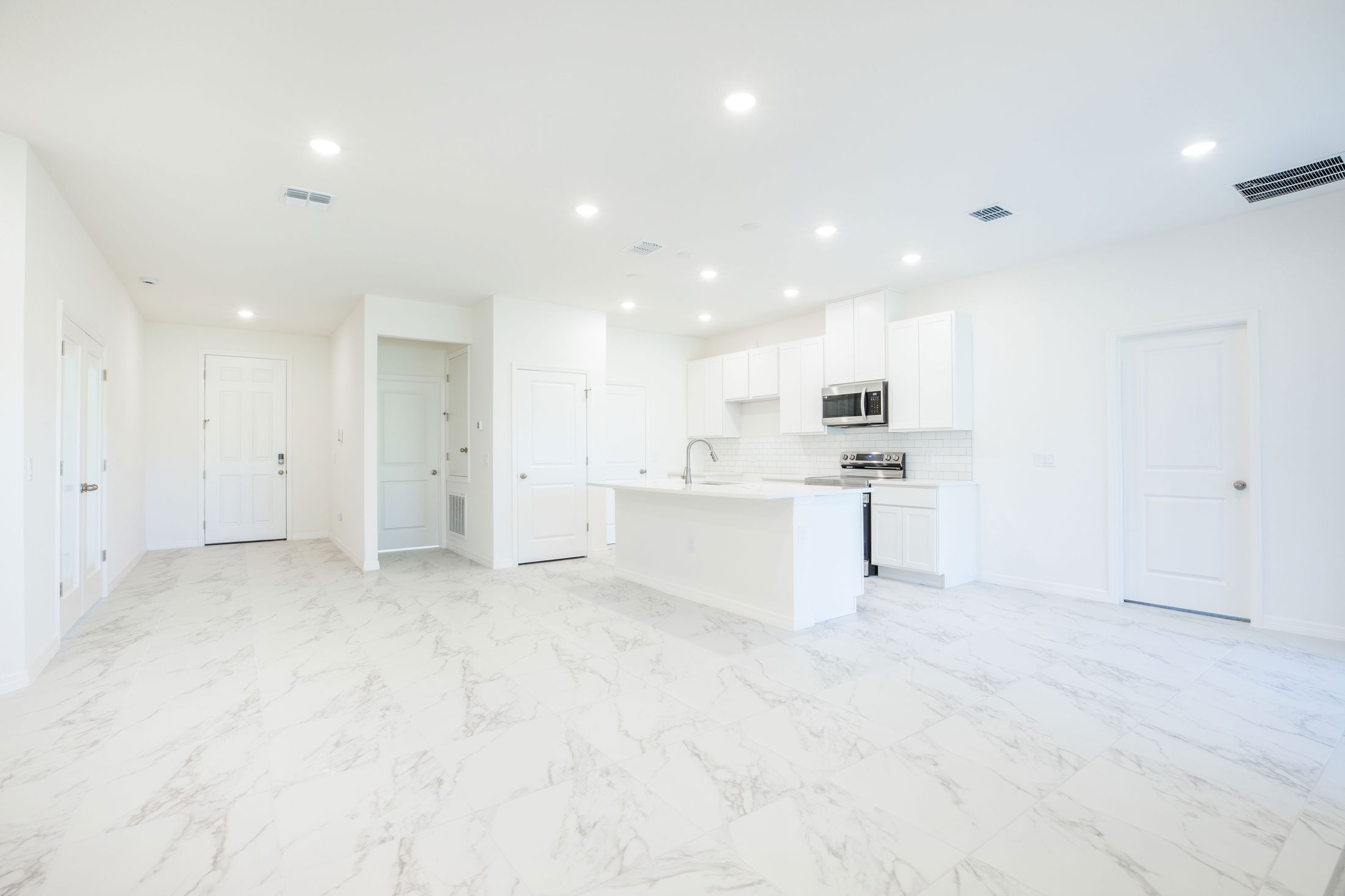 A modern, open-concept kitchen featuring white cabinetry, stainless steel appliances, and marble tile flooring under bright recessed lighting.