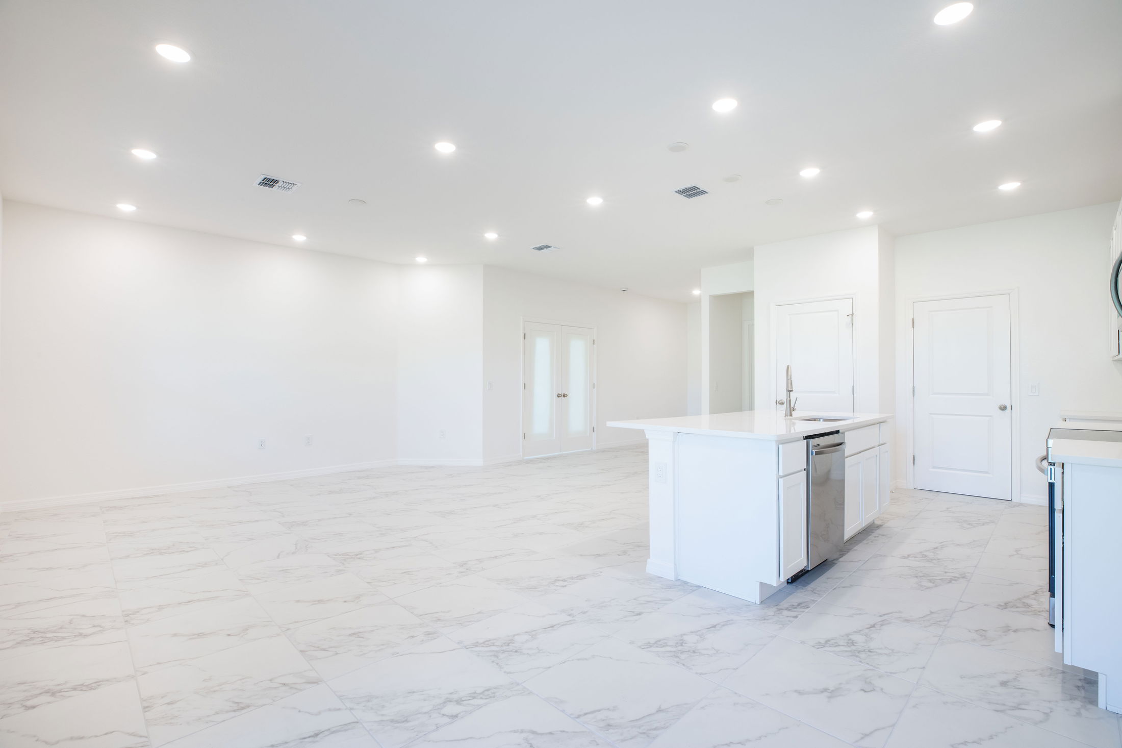 Spacious, modern open-concept kitchen and living area with white marble floors and bright lighting.