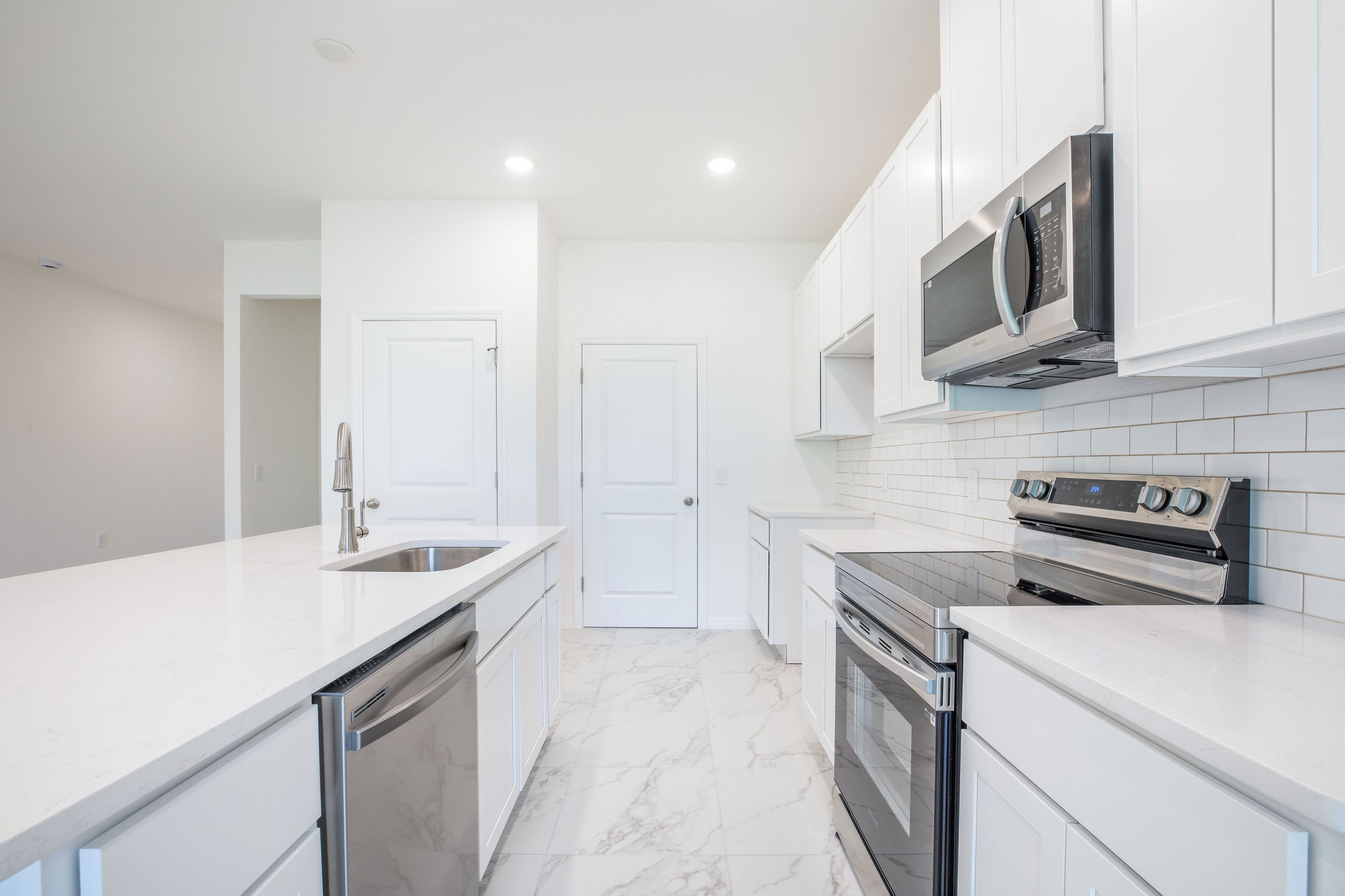 Modern white kitchen with marble countertops, stainless steel appliances, and sleek cabinetry.