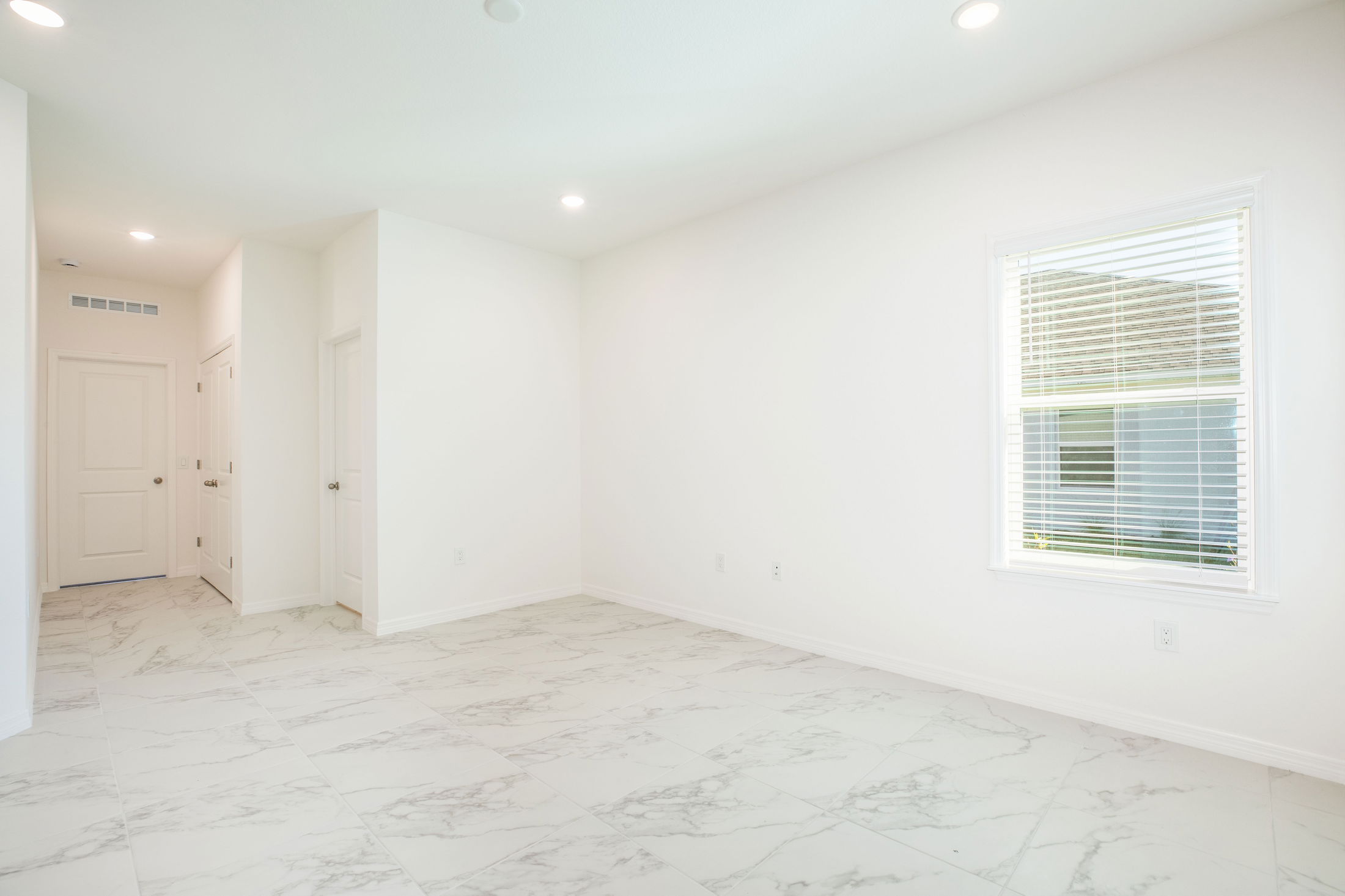 Bright, empty room with white walls, marble-tiled floor, and a single window with blinds.