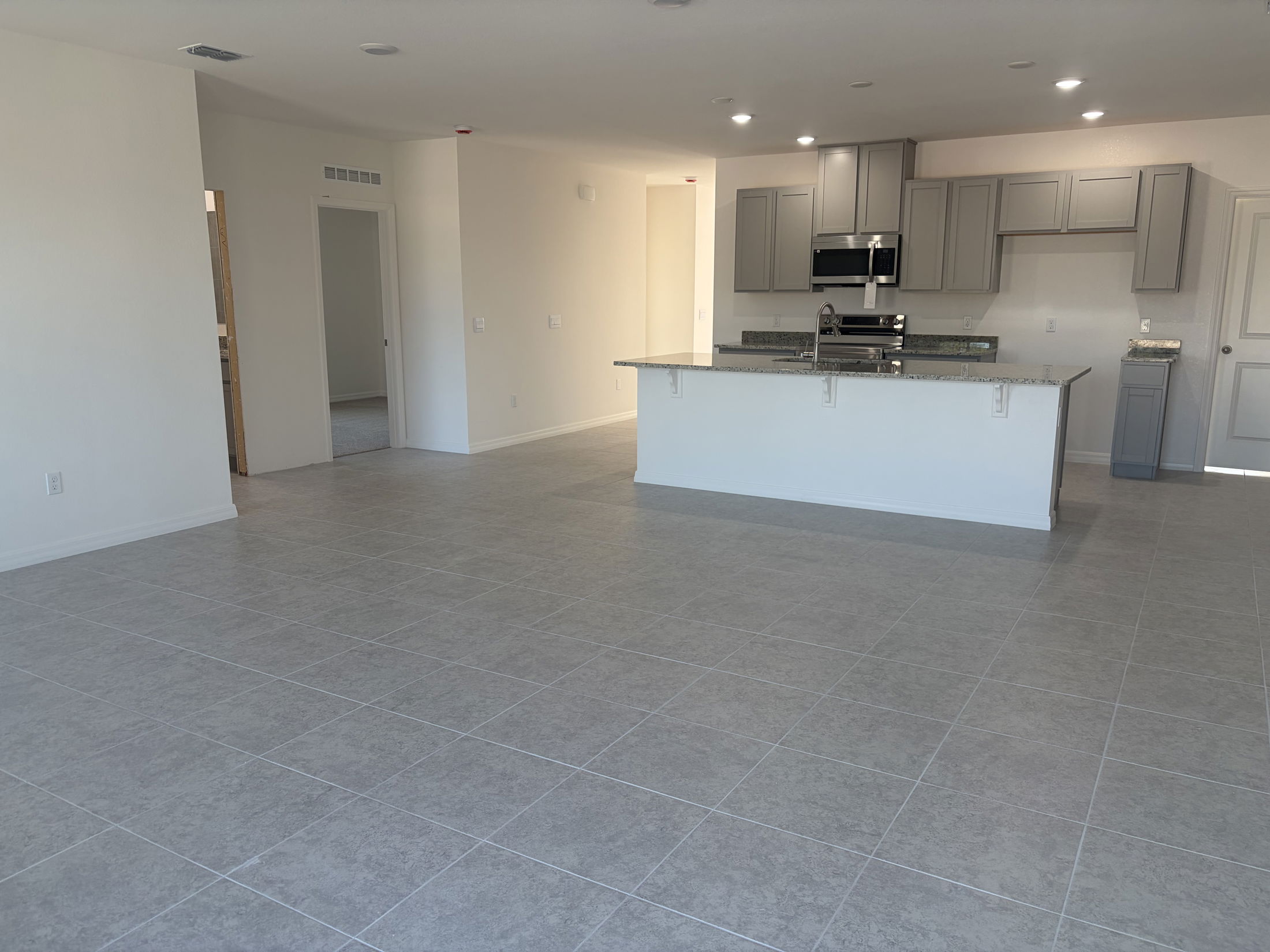 Spacious modern kitchen and living area featuring gray tiled floors and stainless steel appliances in a newly constructed home.