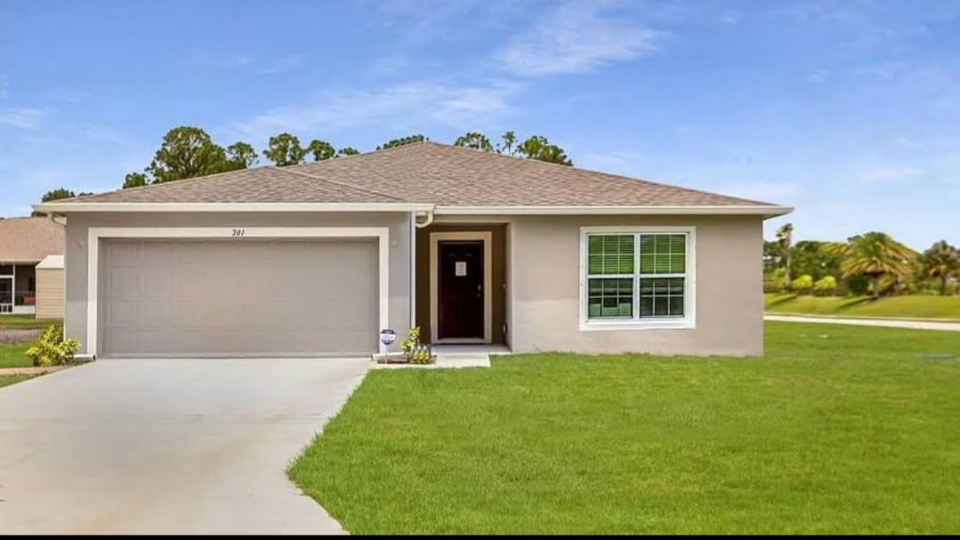 Modern single-story home with a garage, lush green lawn, and large windows under a clear blue sky.