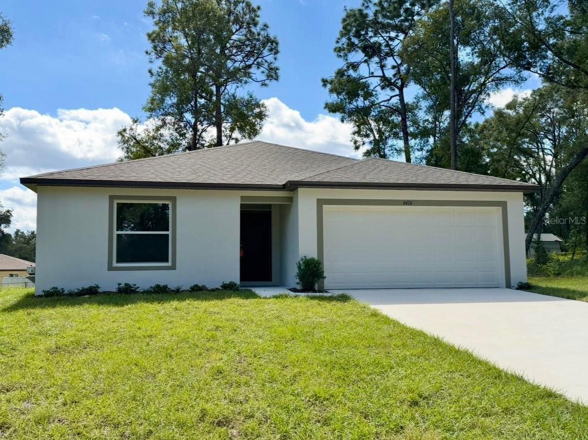 Modern single-family home with a spacious front yard and two-car garage under a blue sky.