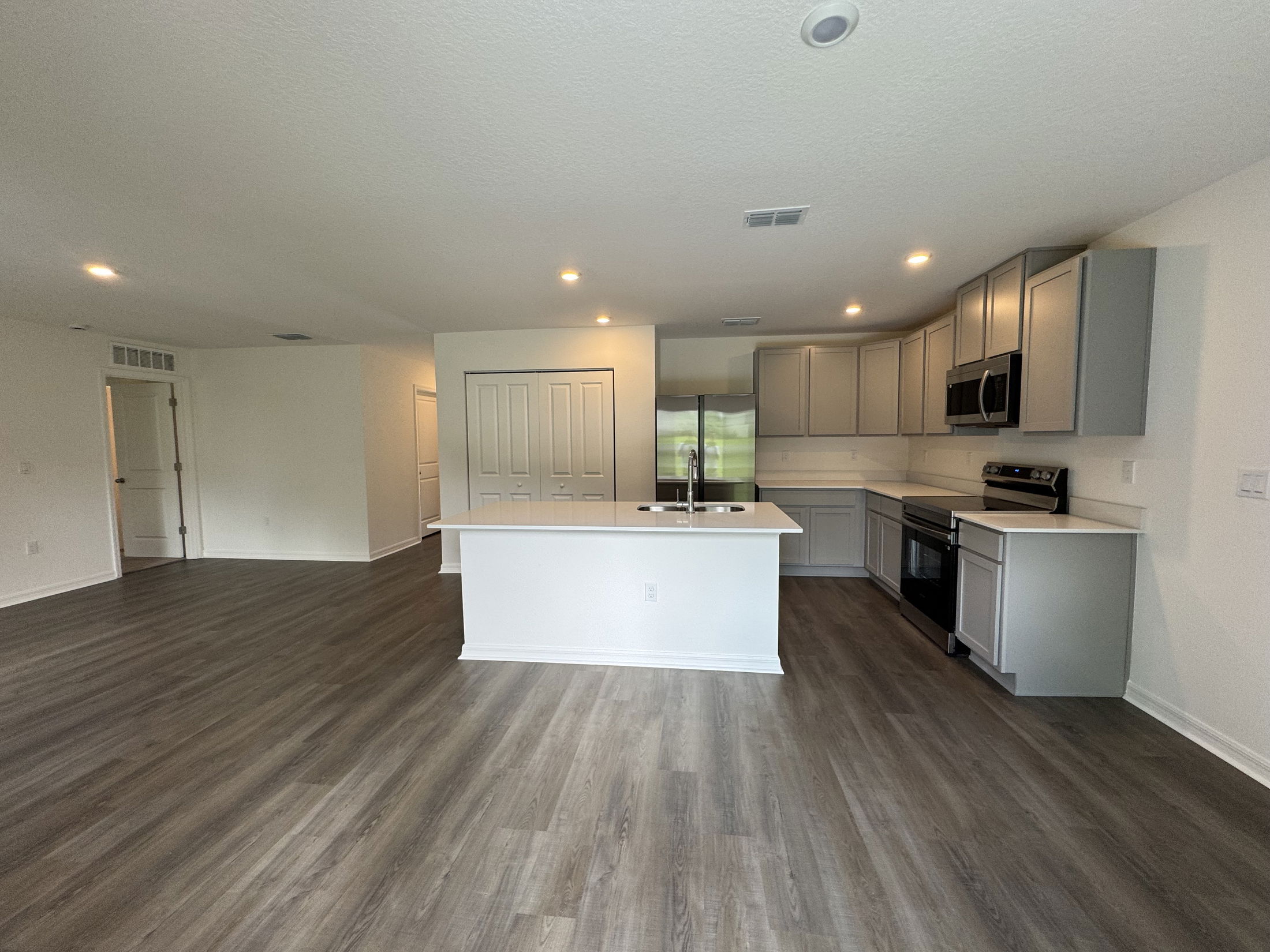 Modern open-concept kitchen and living area featuring stainless steel appliances, gray cabinetry, and hardwood flooring.