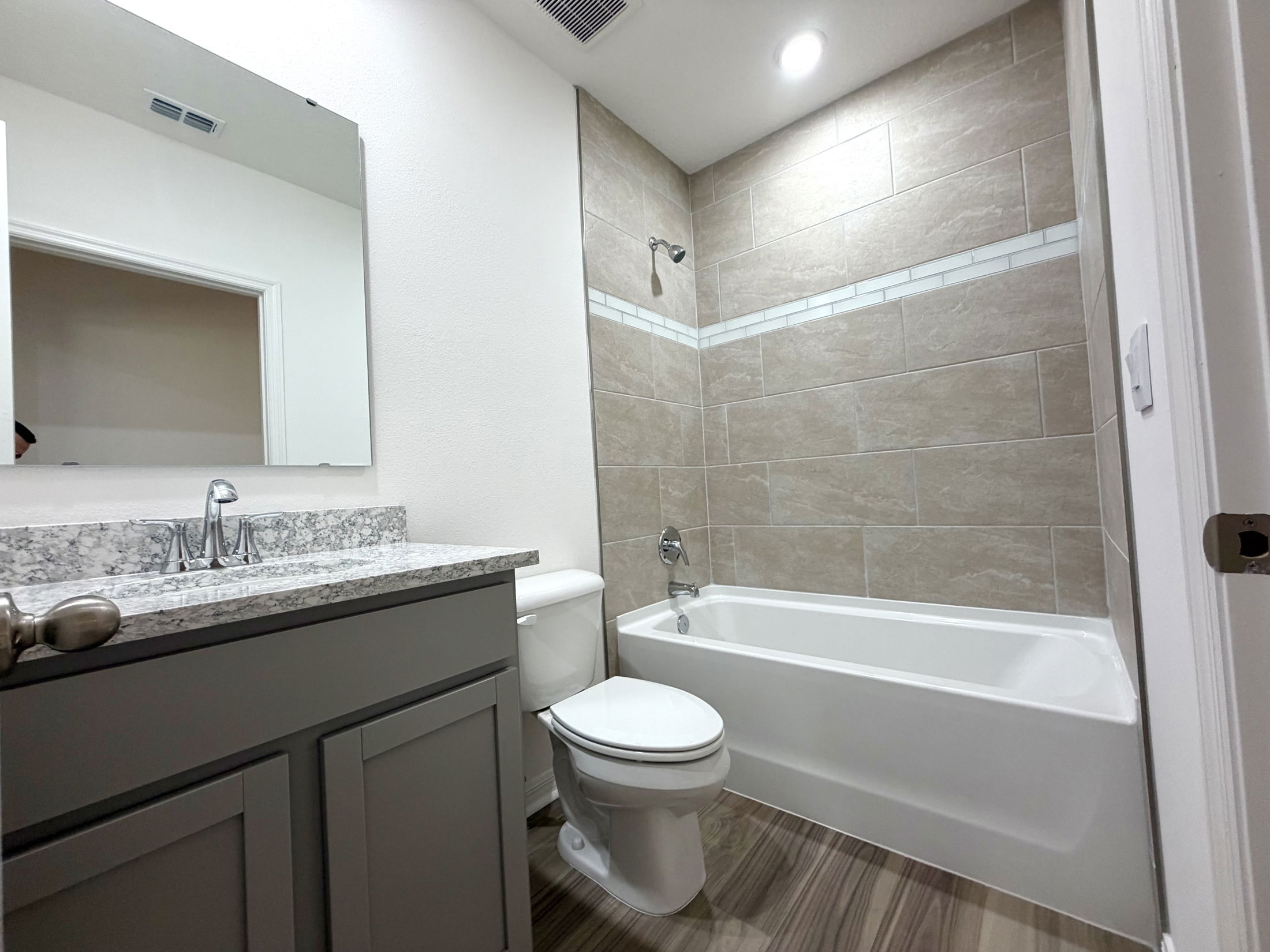 Modern bathroom featuring a gray vanity with a granite countertop, a white bathtub, and tiled walls in neutral tones.