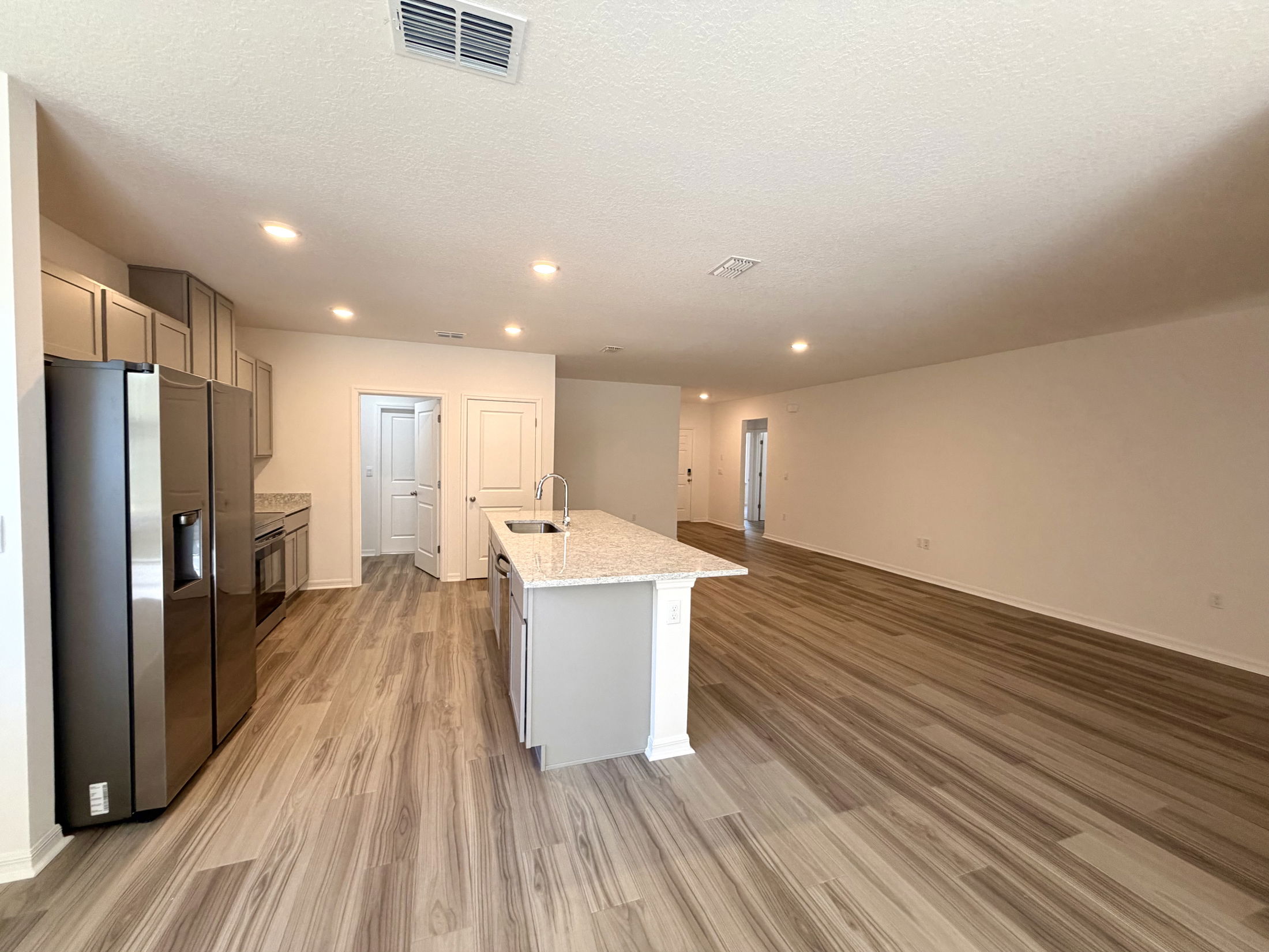 Modern open-concept kitchen and living space featuring stainless steel appliances, granite countertops, and laminate flooring.