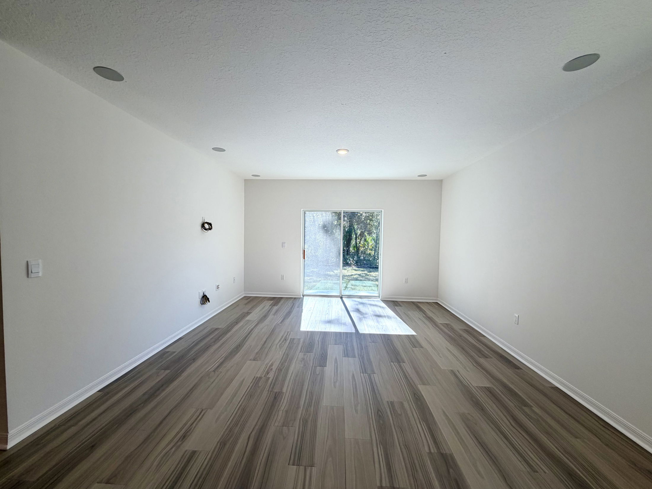 Spacious and modern living room with large windows and beautiful wood-like flooring, ideal for bright natural light.