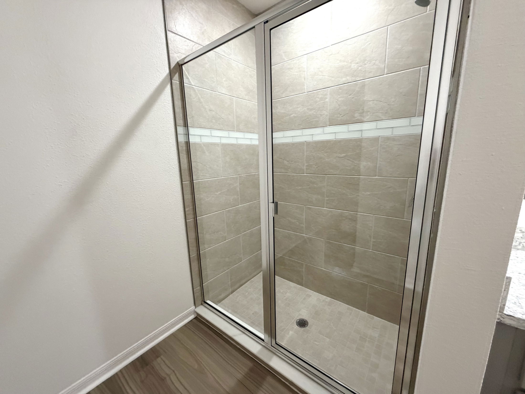 Modern walk-in shower with glass doors and beige tile accents in a spacious bathroom.