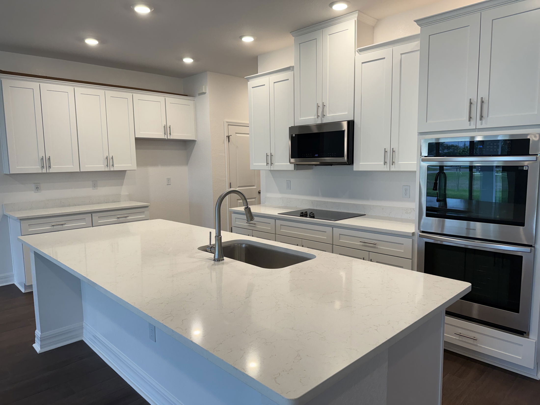 Modern kitchen featuring white cabinetry, quartz countertops, stainless steel appliances, and recessed lighting.