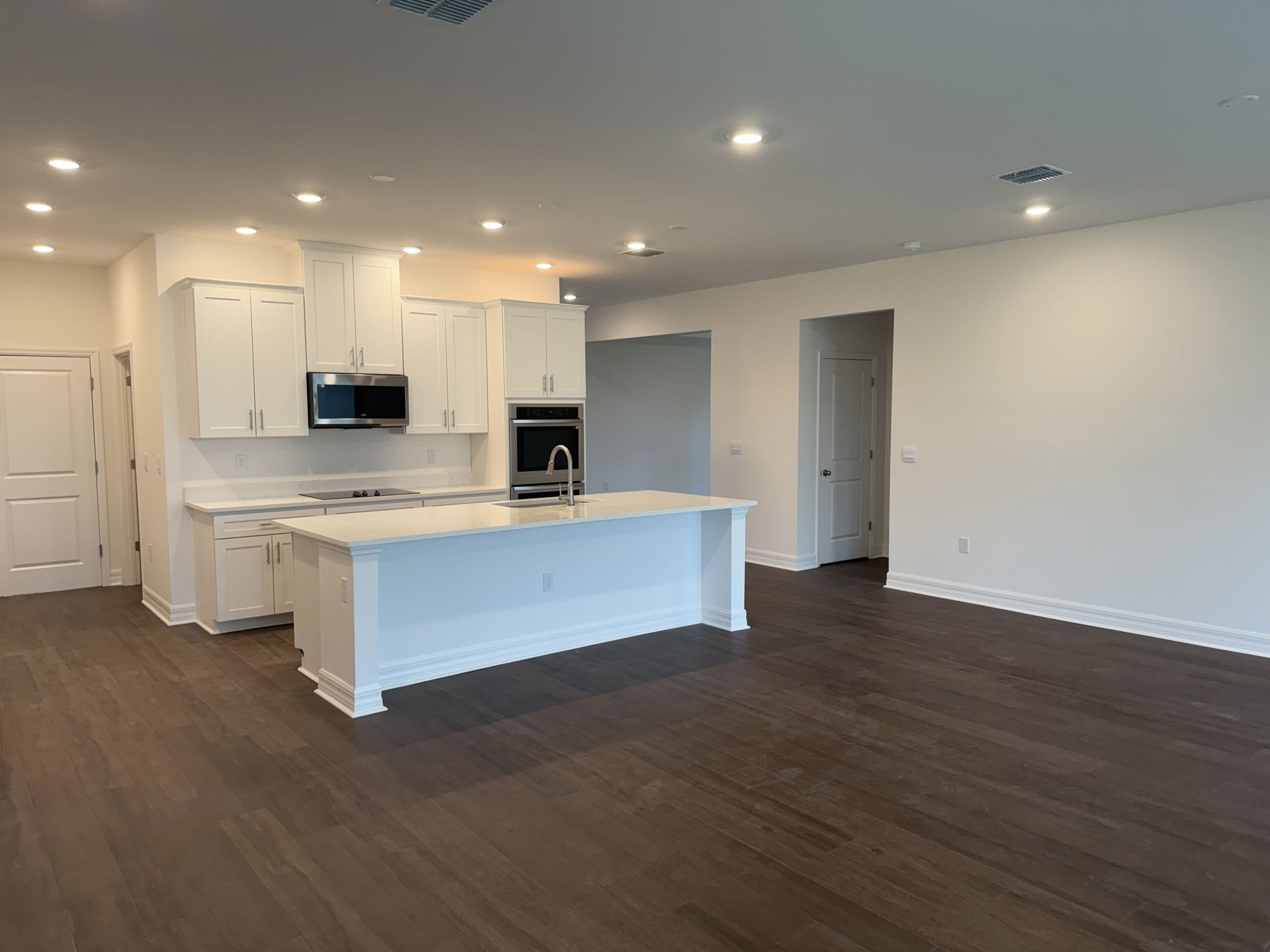 Modern kitchen with white cabinets, stainless steel appliances, and hardwood flooring in a spacious open-concept layout.