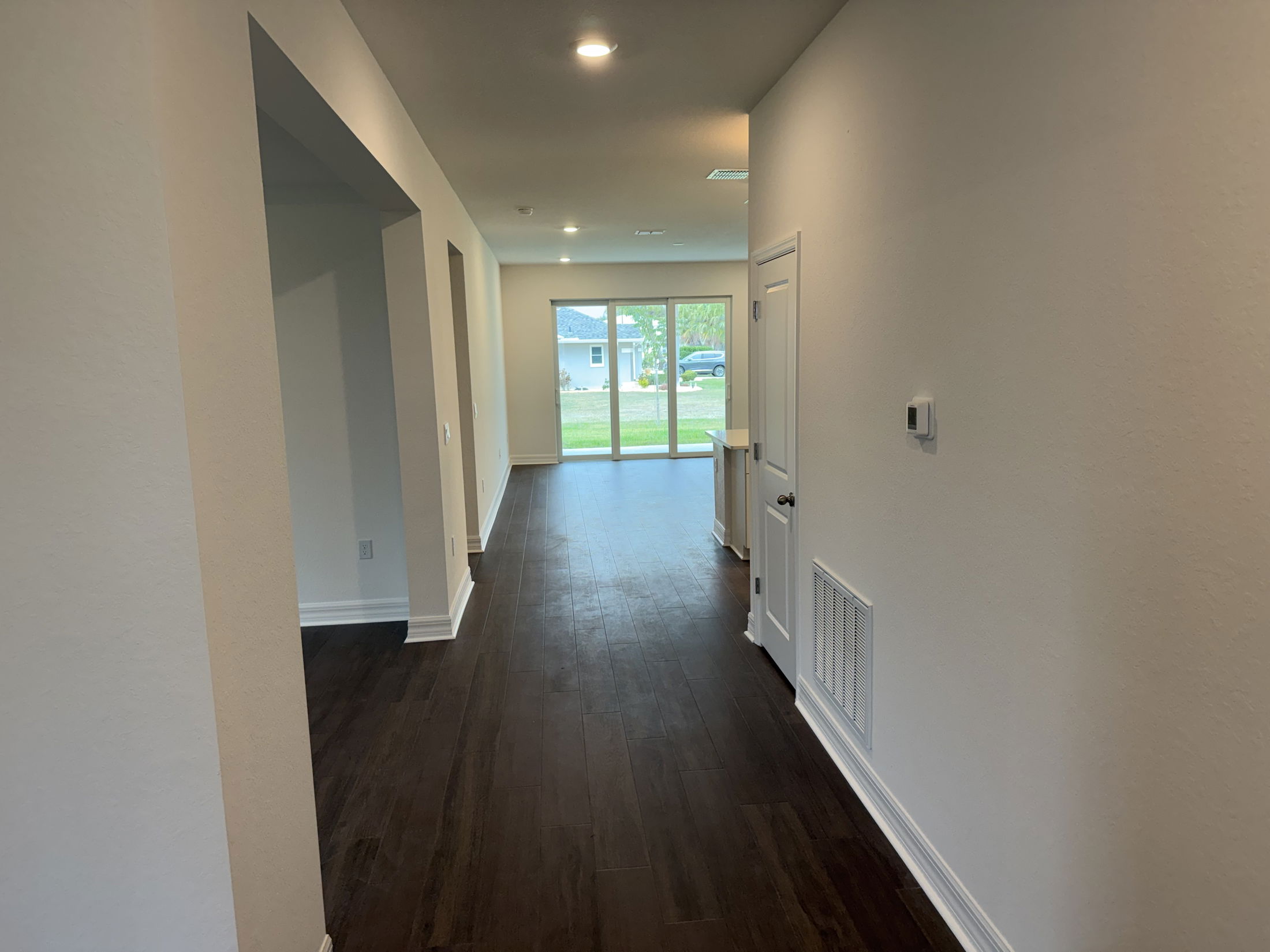 A modern hallway with wooden floors and natural light, featuring white walls and an entrance to the outside in a contemporary home.