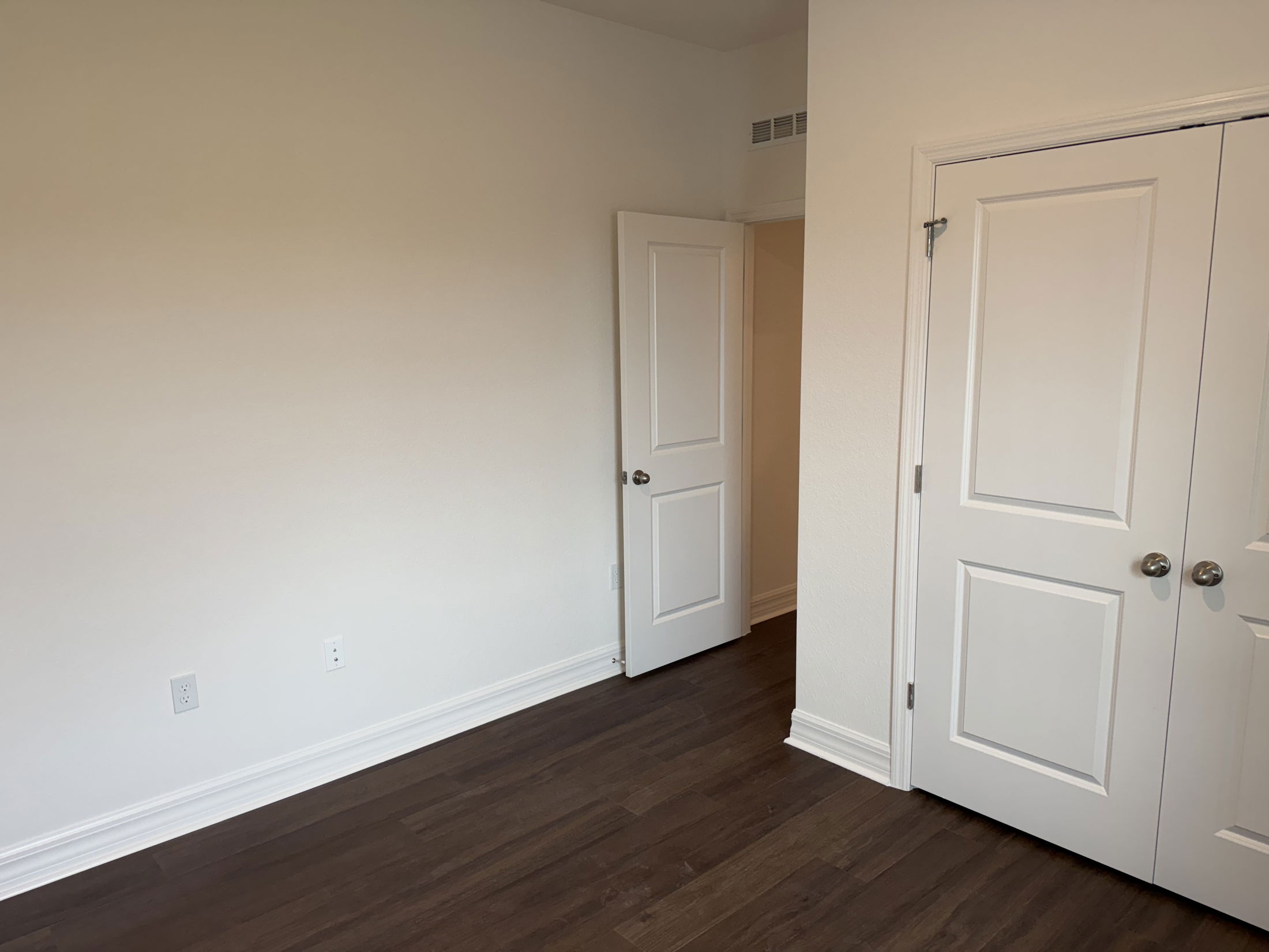 A clean and spacious bedroom interior featuring white walls, dark wood flooring, and two closets.