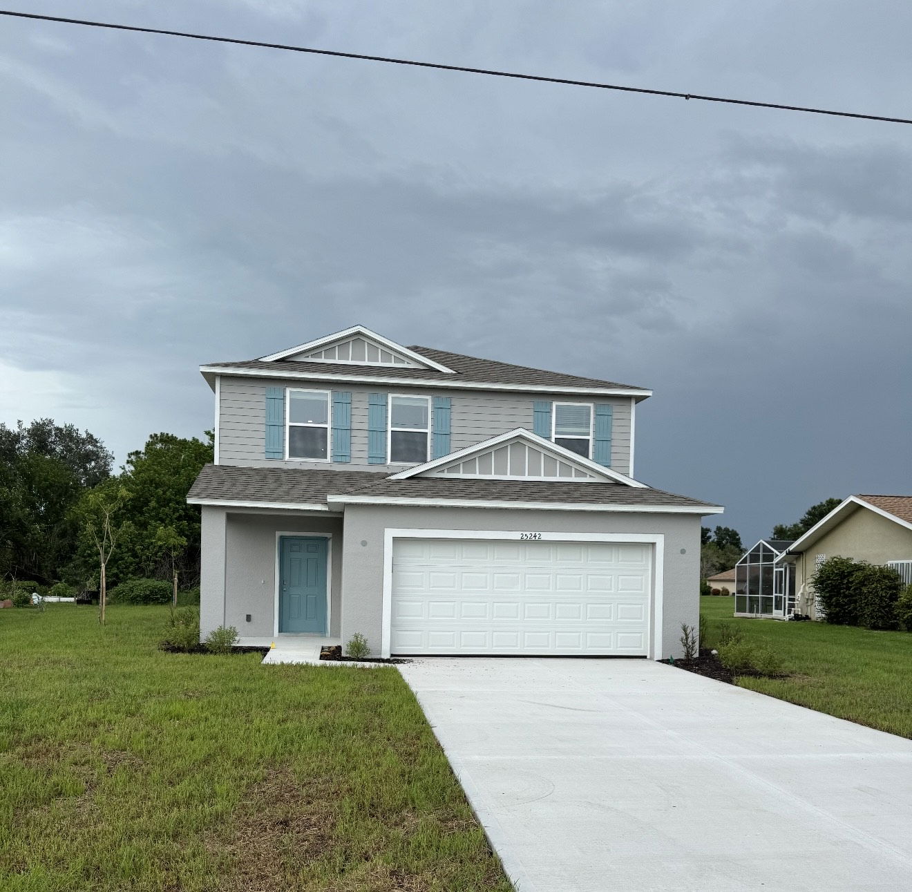 Modern two-story suburban house with a blue door, white garage, and manicured lawn under a cloudy sky.