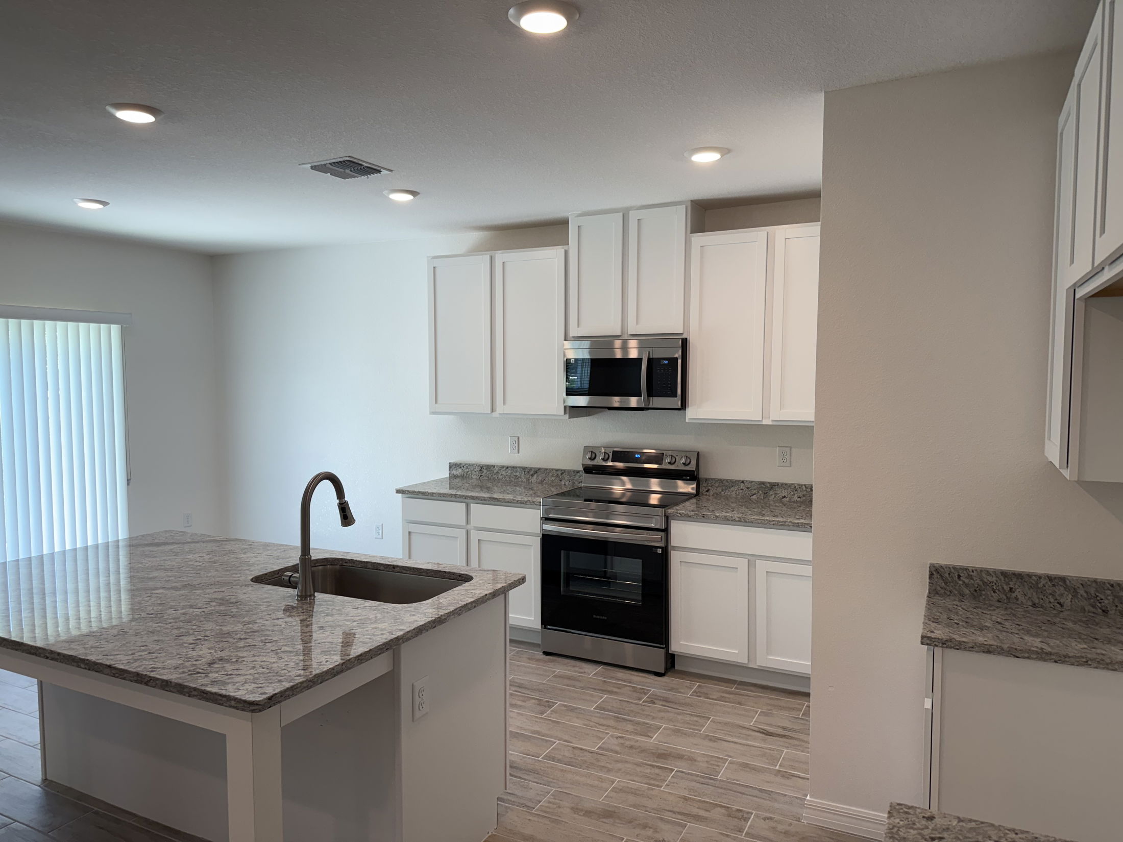 Modern kitchen with white cabinets, granite countertops, stainless steel appliances, and recessed lighting.