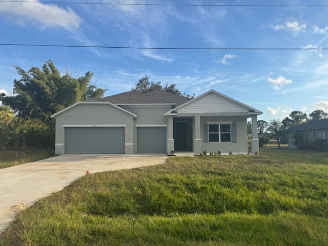 Modern gray single-story house with a three-car garage and a large driveway under a clear blue sky.