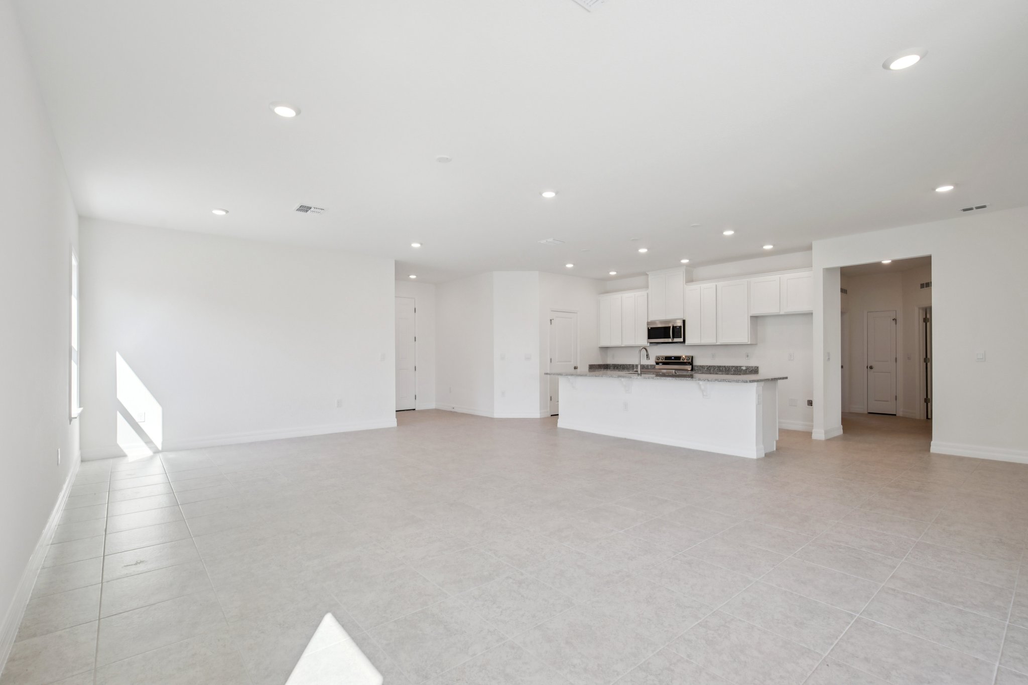 Spacious modern open-concept living room and kitchen with white walls and tile flooring.
