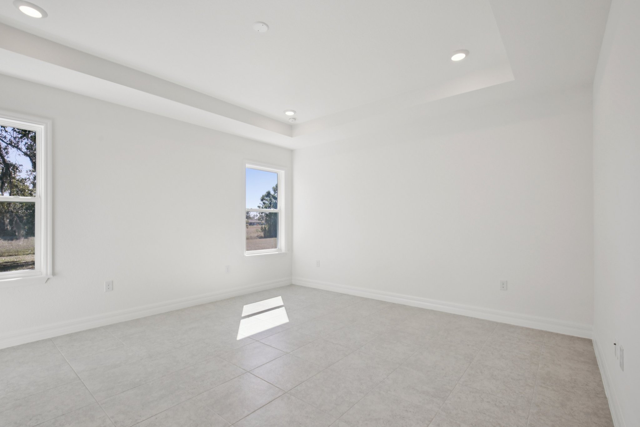 Spacious and bright empty room featuring large windows, neutral wall colors, and modern tile flooring.