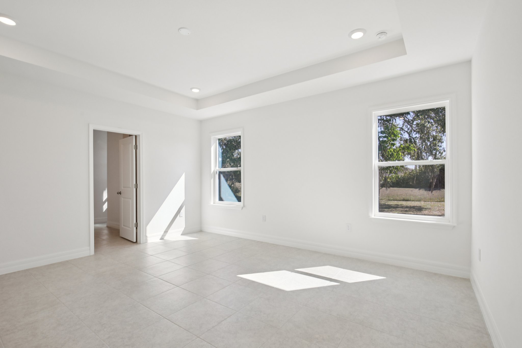 Spacious white room with large windows allowing natural light and tiled flooring.