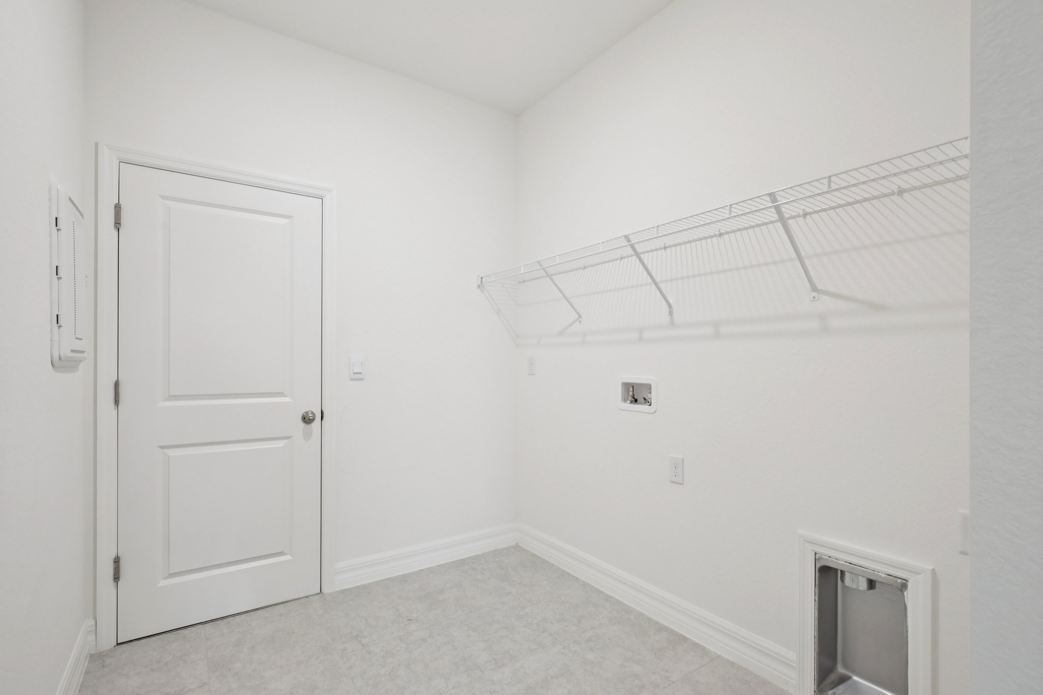 Bright and minimalist laundry room featuring a white door, wall shelf, and tiled floor.