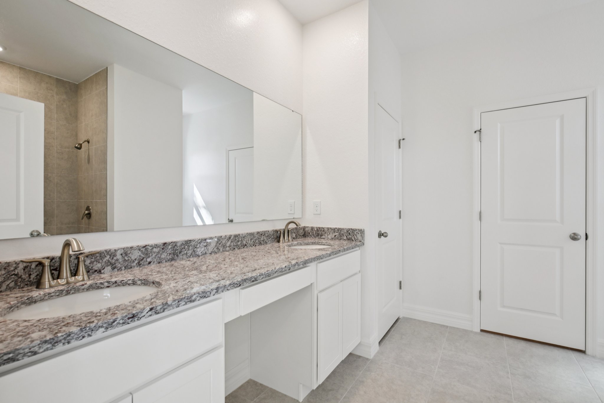 Modern bathroom interior featuring a double vanity with granite countertop, large mirror, and tiled shower area.