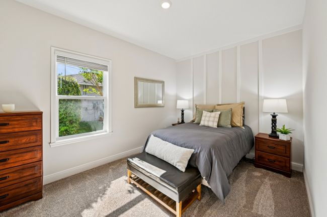 Bright and cozy bedroom with a neatly made bed, wooden nightstands, a bench, and a window letting in natural light.