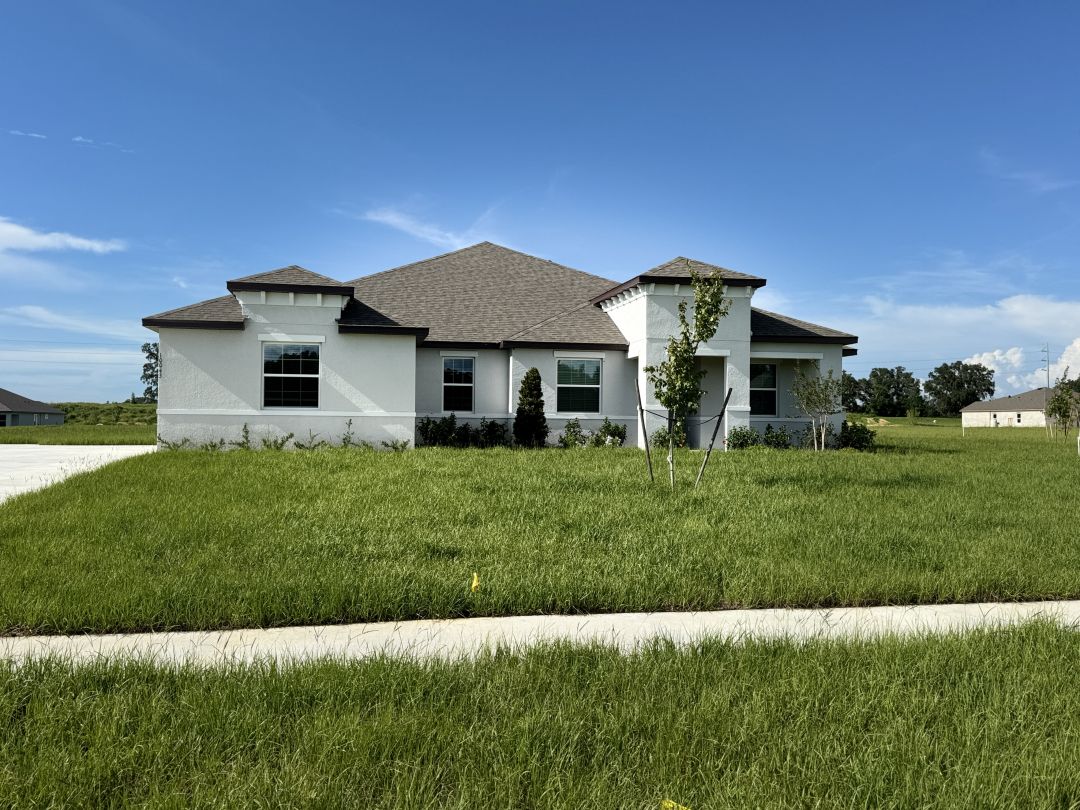 Modern single-story white house with gabled roof nestled in a lush green lawn under a clear blue sky.