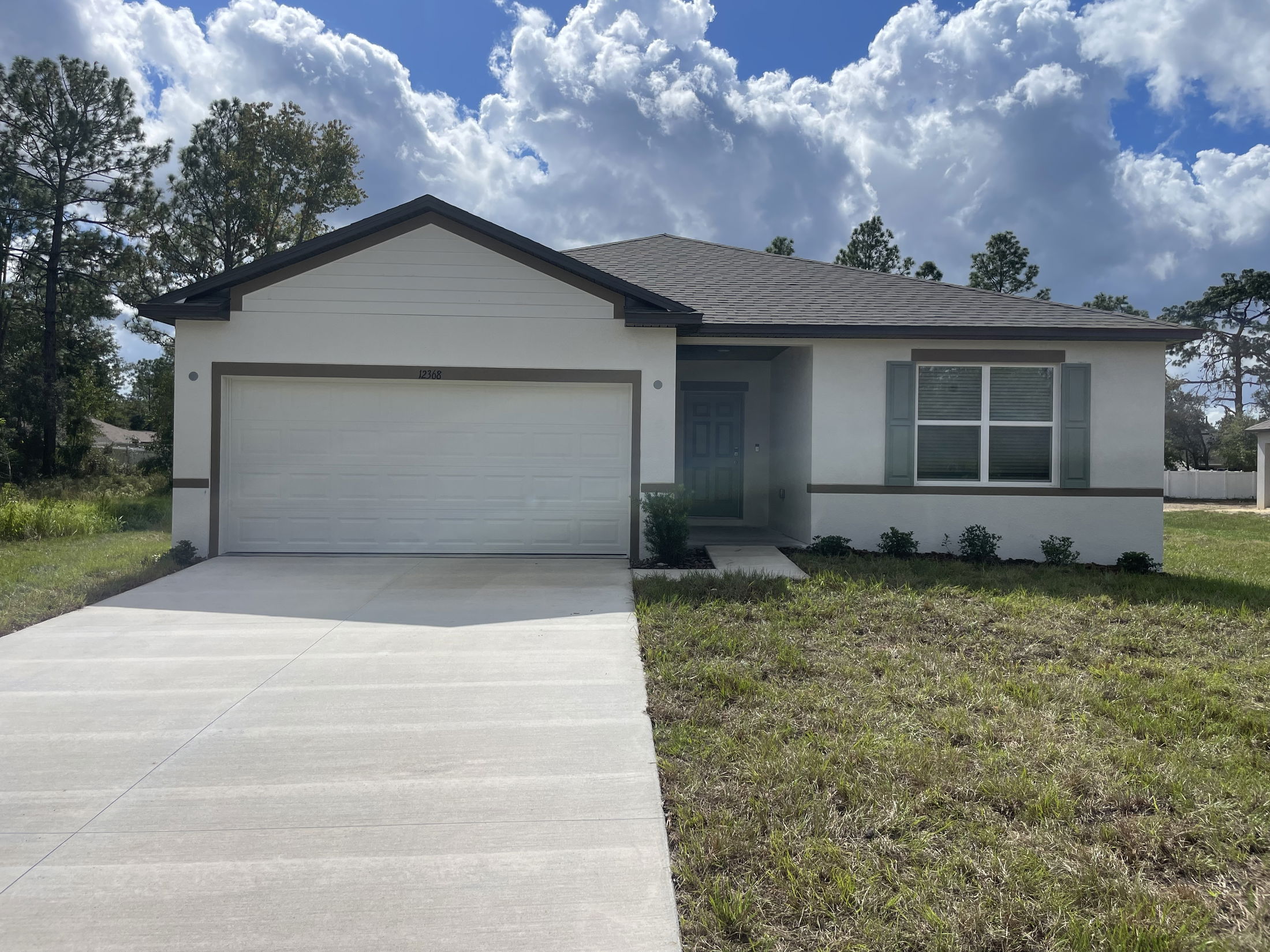 Modern single-story home with a spacious front yard, garage, and cloudy blue sky.