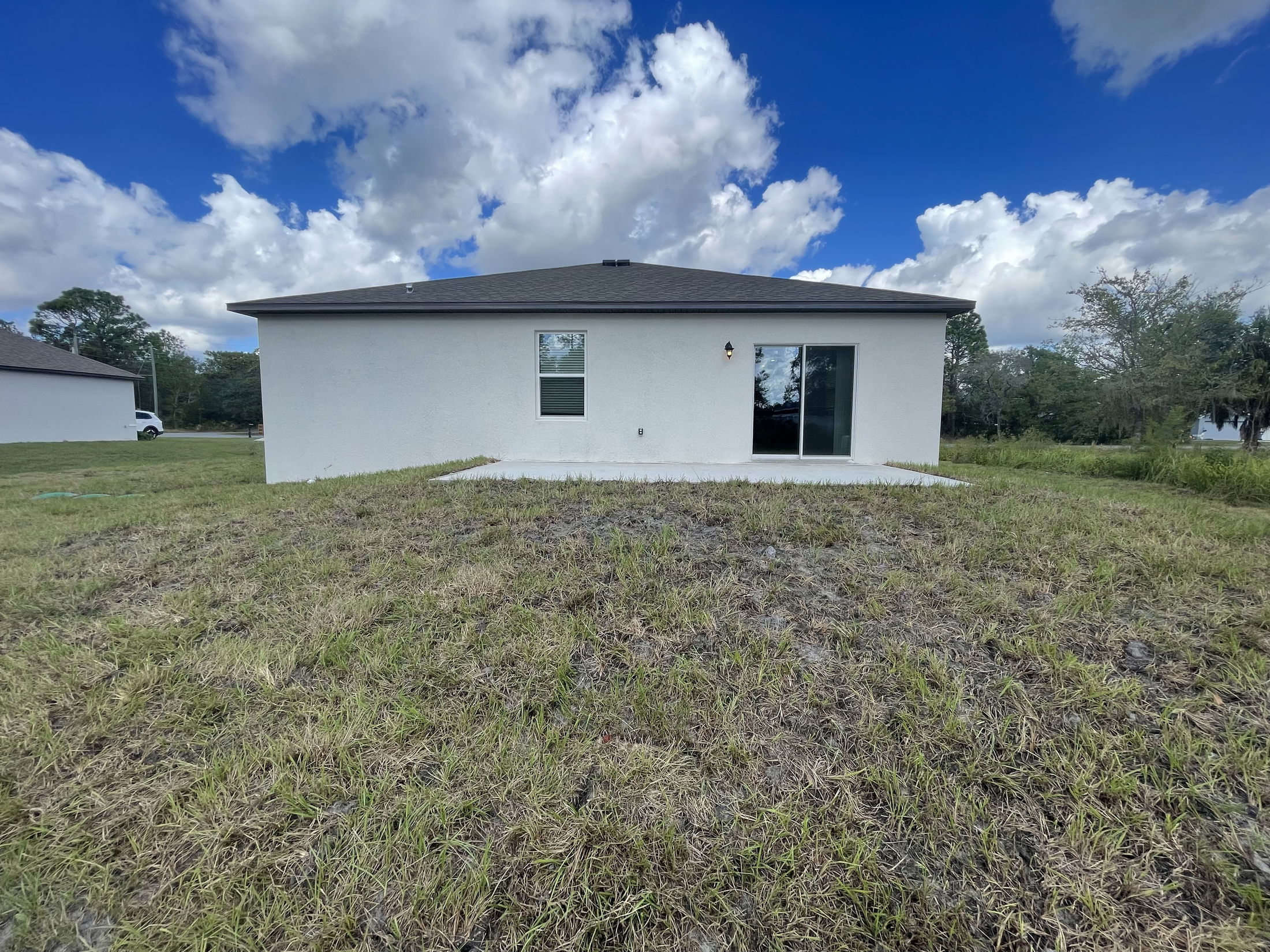 Backyard view of a modern white house with a patio, under a blue sky with clouds.