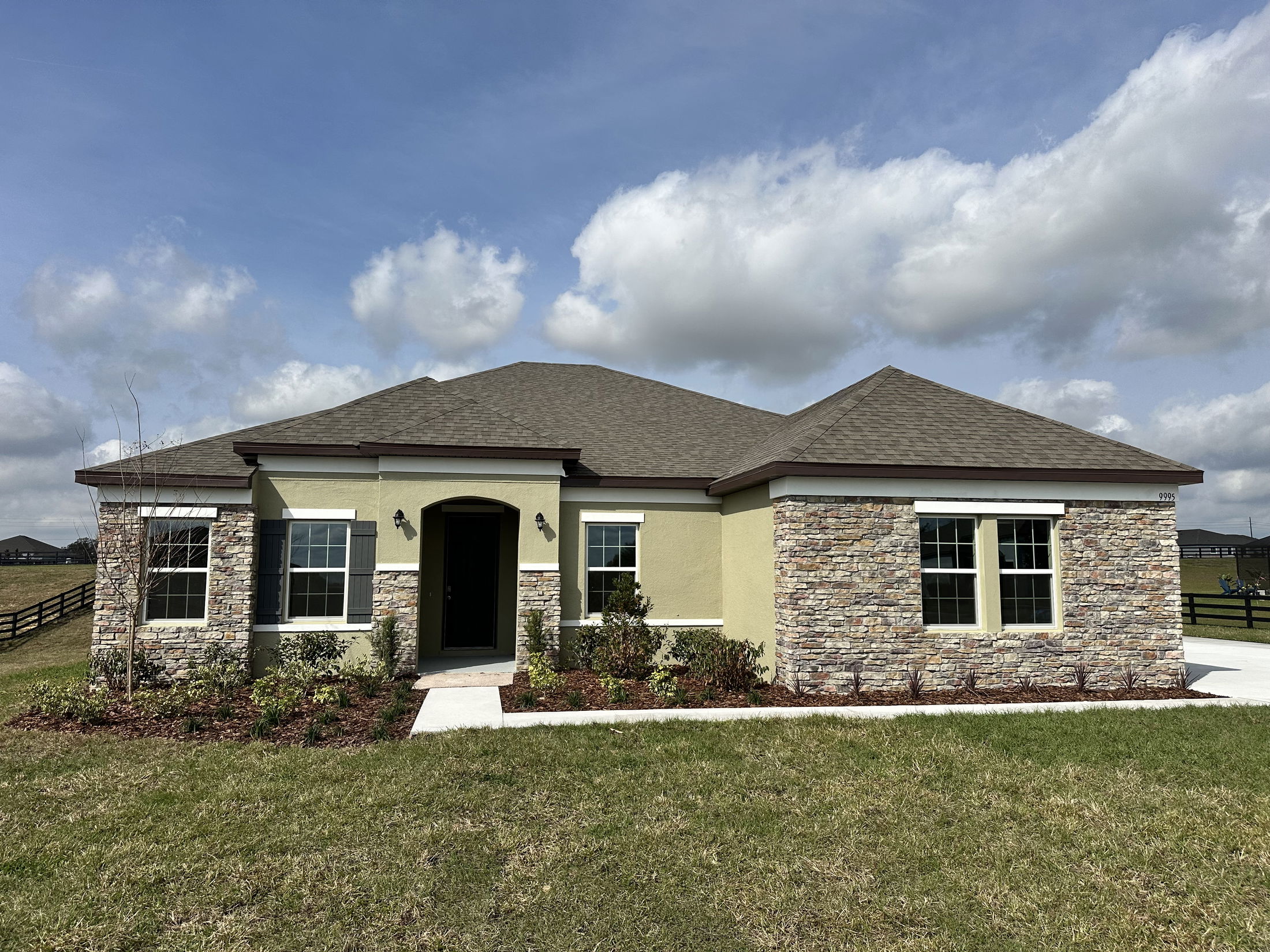 A modern single-story house with stone and stucco exterior, featuring multiple windows and a well-kept lawn.