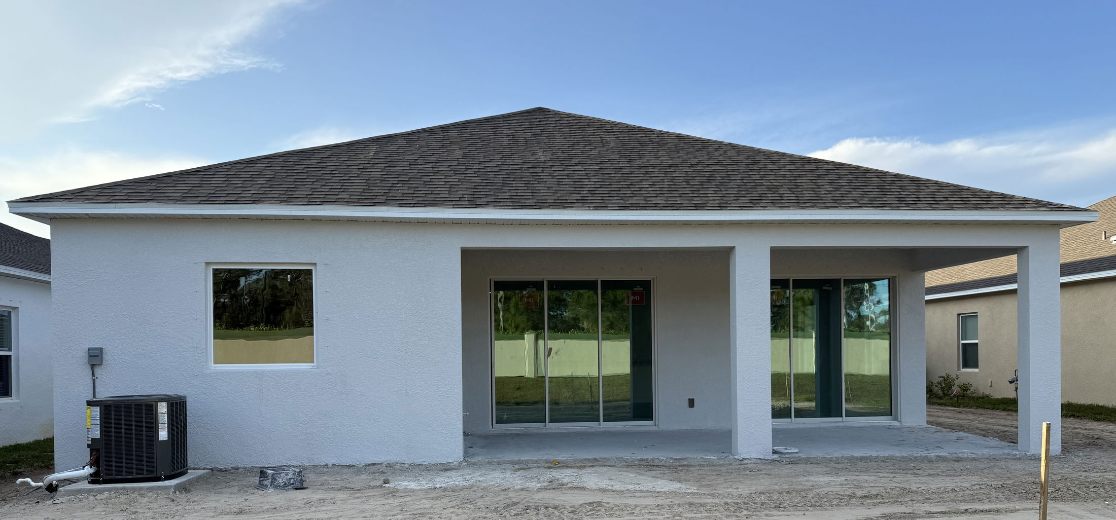 Rear view of a newly constructed house featuring sliding glass doors and an outdoor air conditioning unit against a clear blue sky.