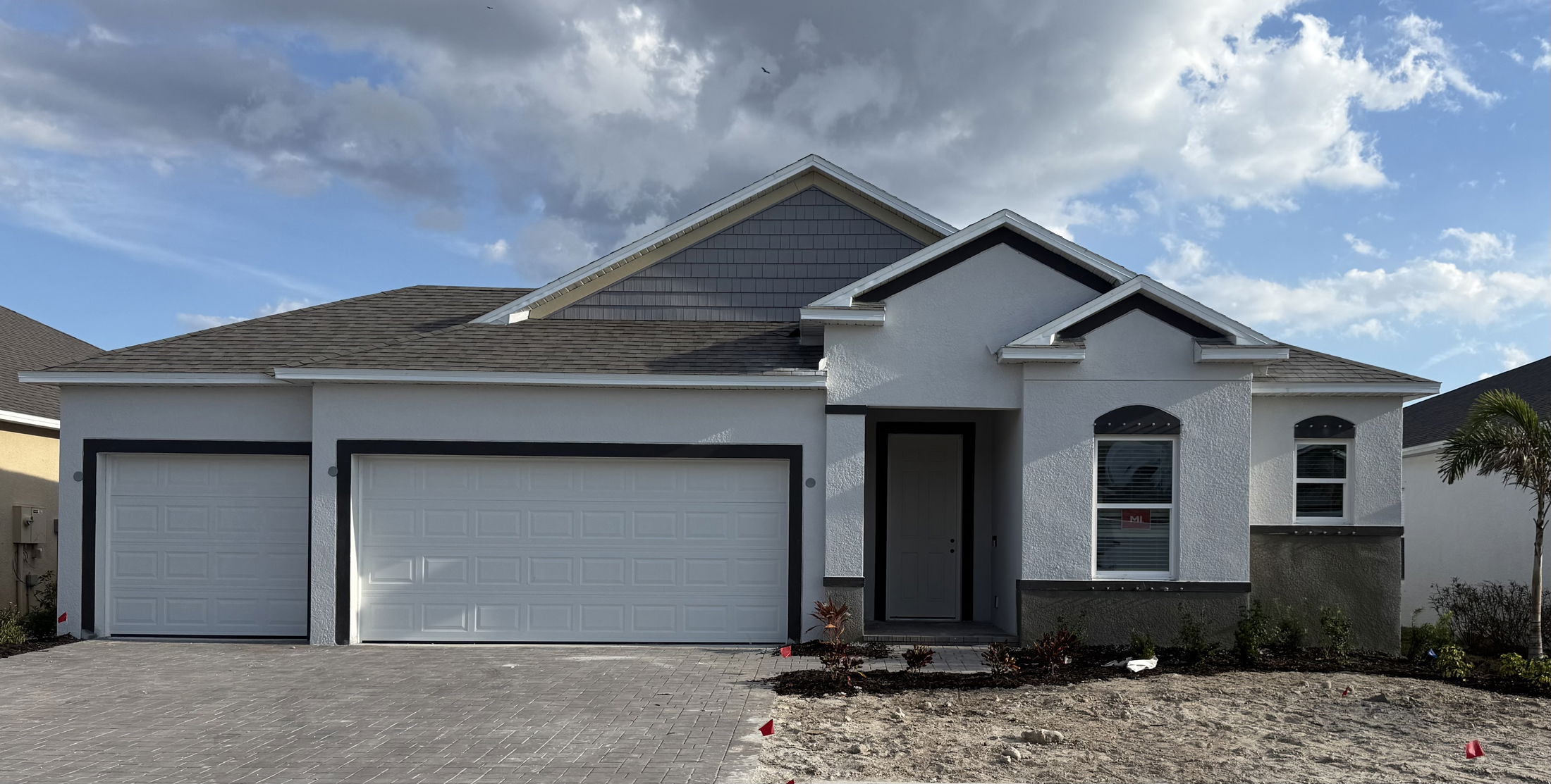 Newly constructed modern single-story home with a three-car garage and gray roof under a partly cloudy sky.